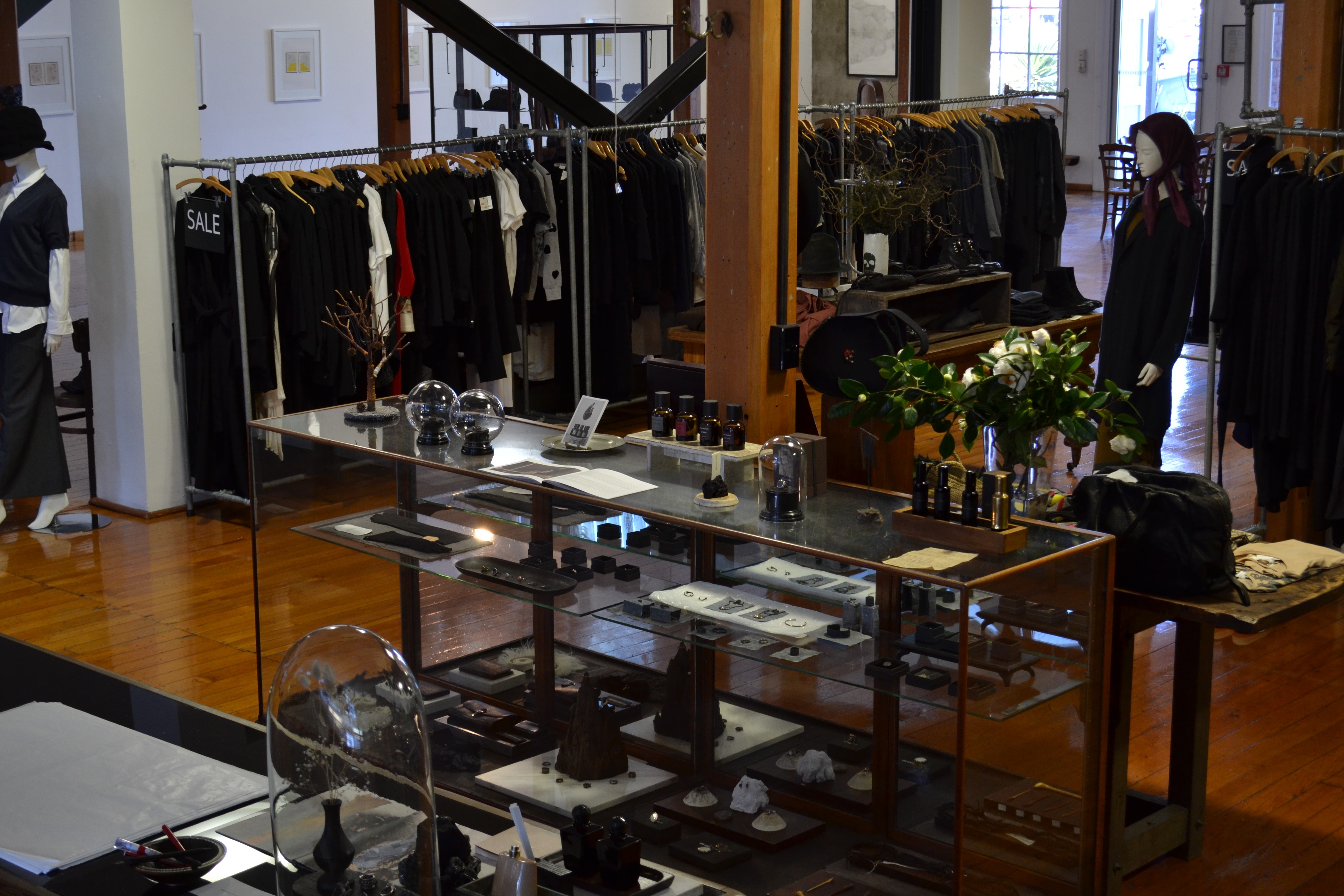 A shop with a wooden floor with clothes and a glass case with objects inside
