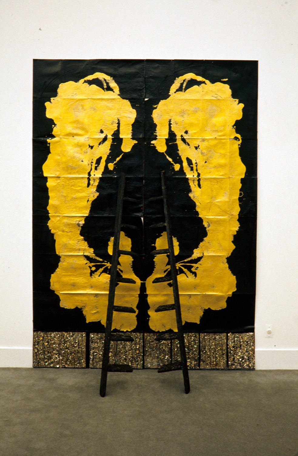 A large black and gold painting with a black ladder-like sculpture leaning against it.