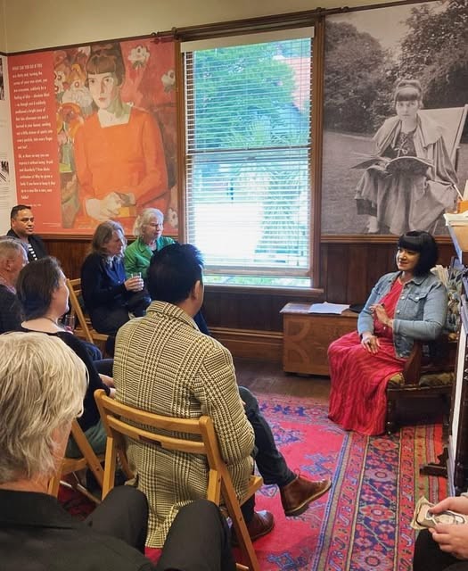 A person speaking to a seated crowd in the room of a museum