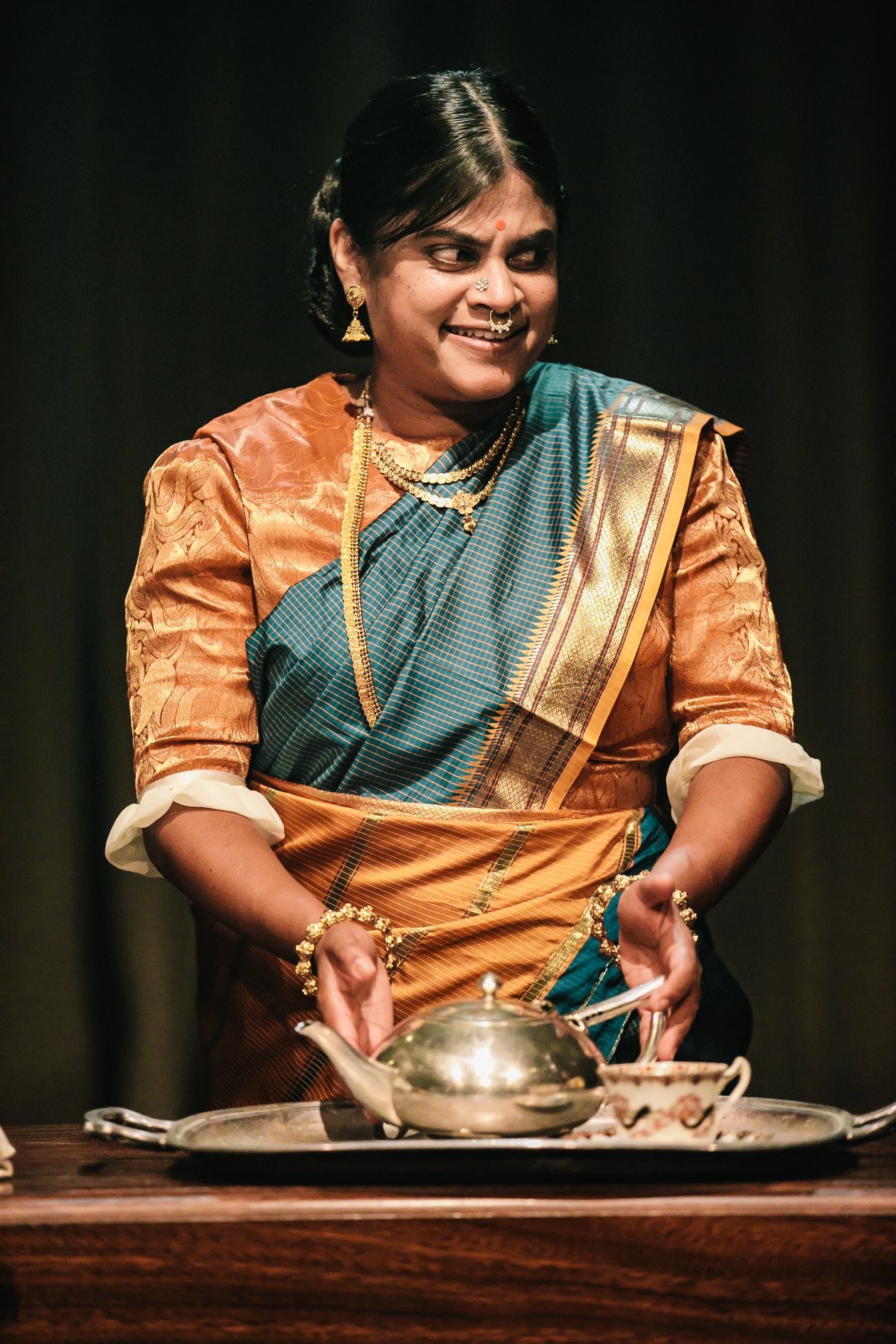 A person in a saree standing behind a teapot