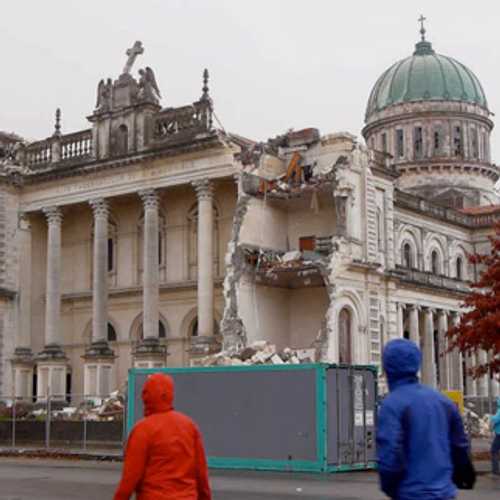 In a scene from the documentary ‘Moving’, three people in raincoats walk past an earthquake-damaged historical building in central Christchurch, New Zealand.