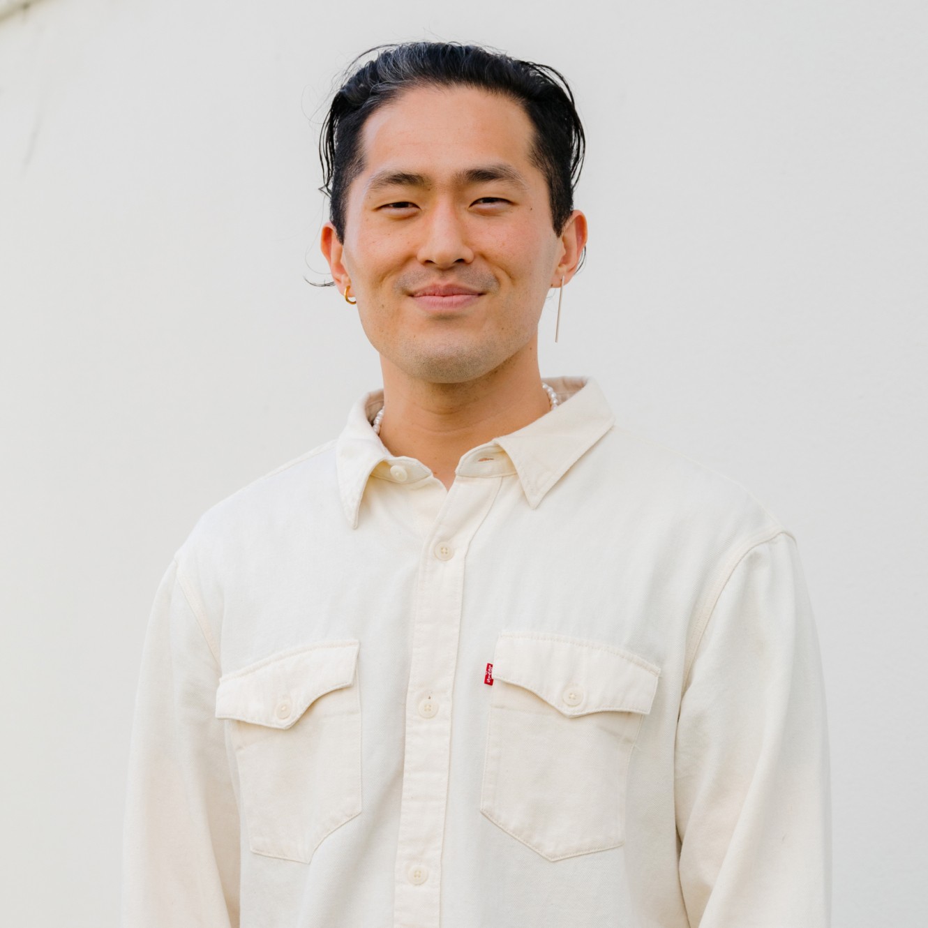 Man with dark hair wearing a cream shirt smiling.