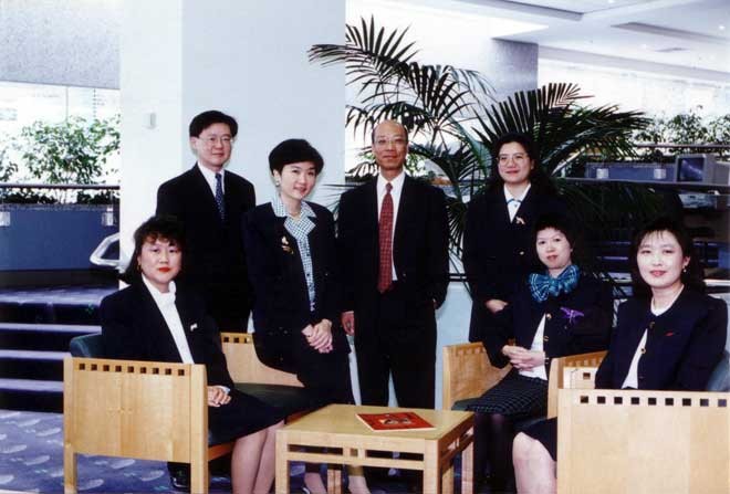 A group of Asian people in corporate outfits sit and stand for a photograph, inside an office.