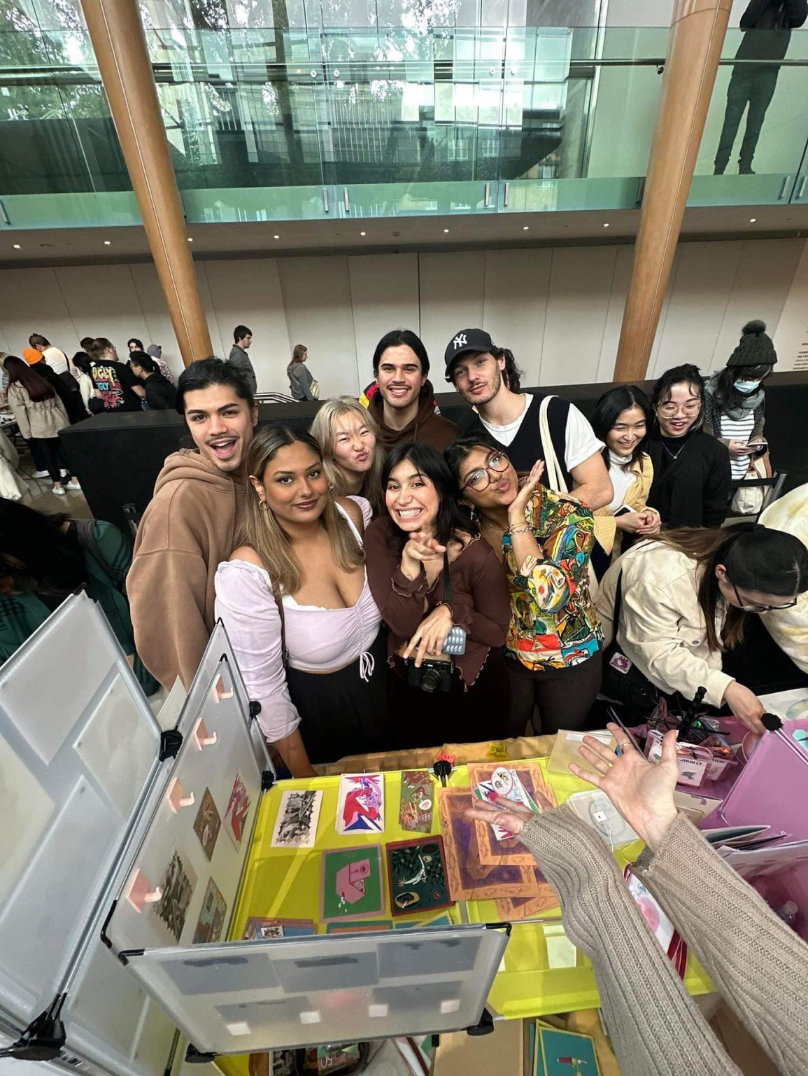 A group of people smiling in front of zine table with various colourful zines and prints. 