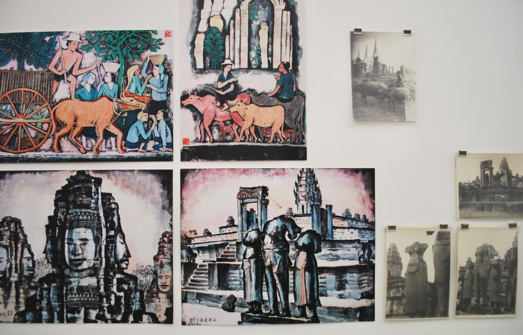 Photos of Angkor pinned to a wall alongside paintings of similar views.