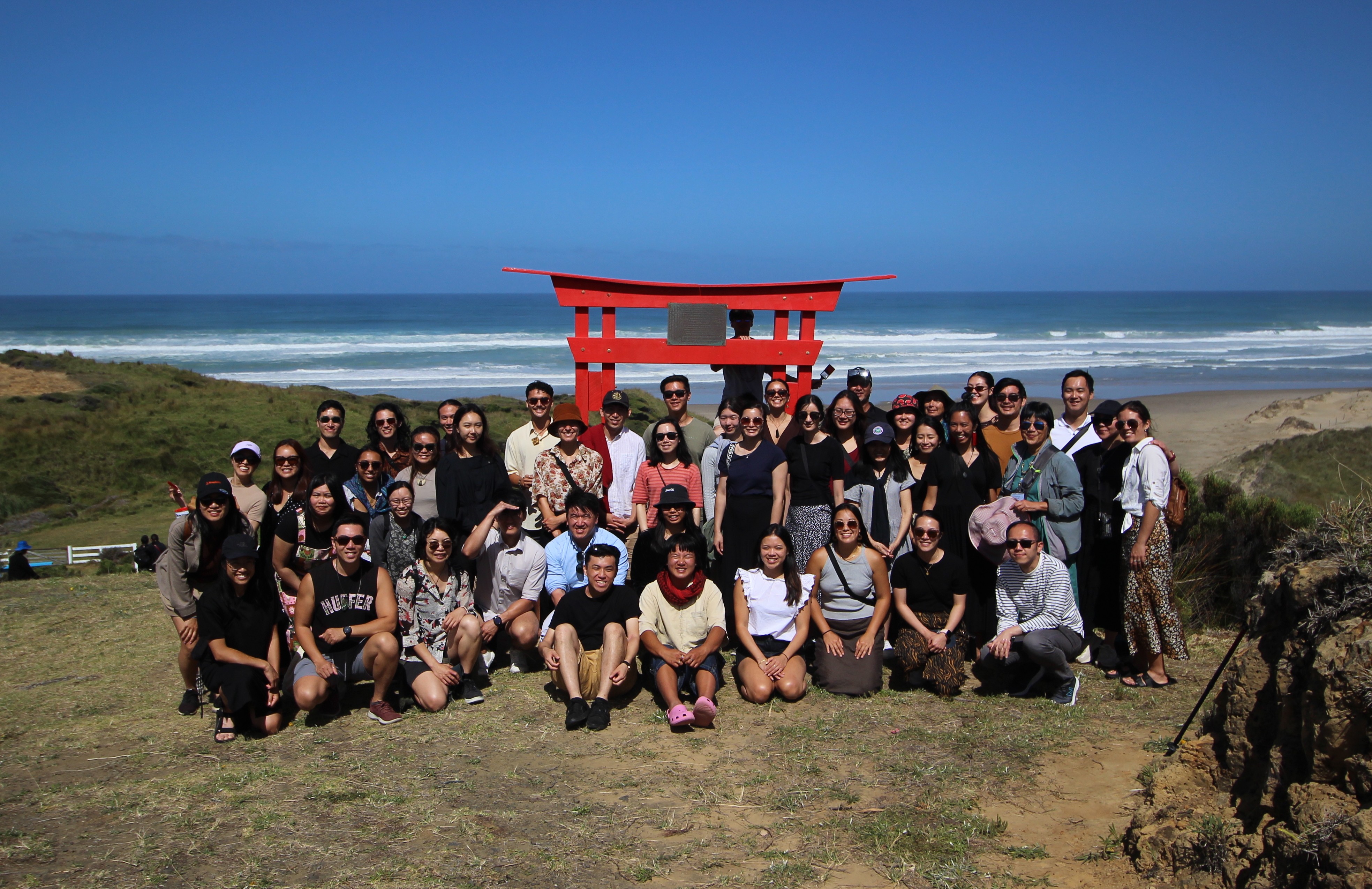 Group of people standing in front of a red arch on a hill with the sea in the background