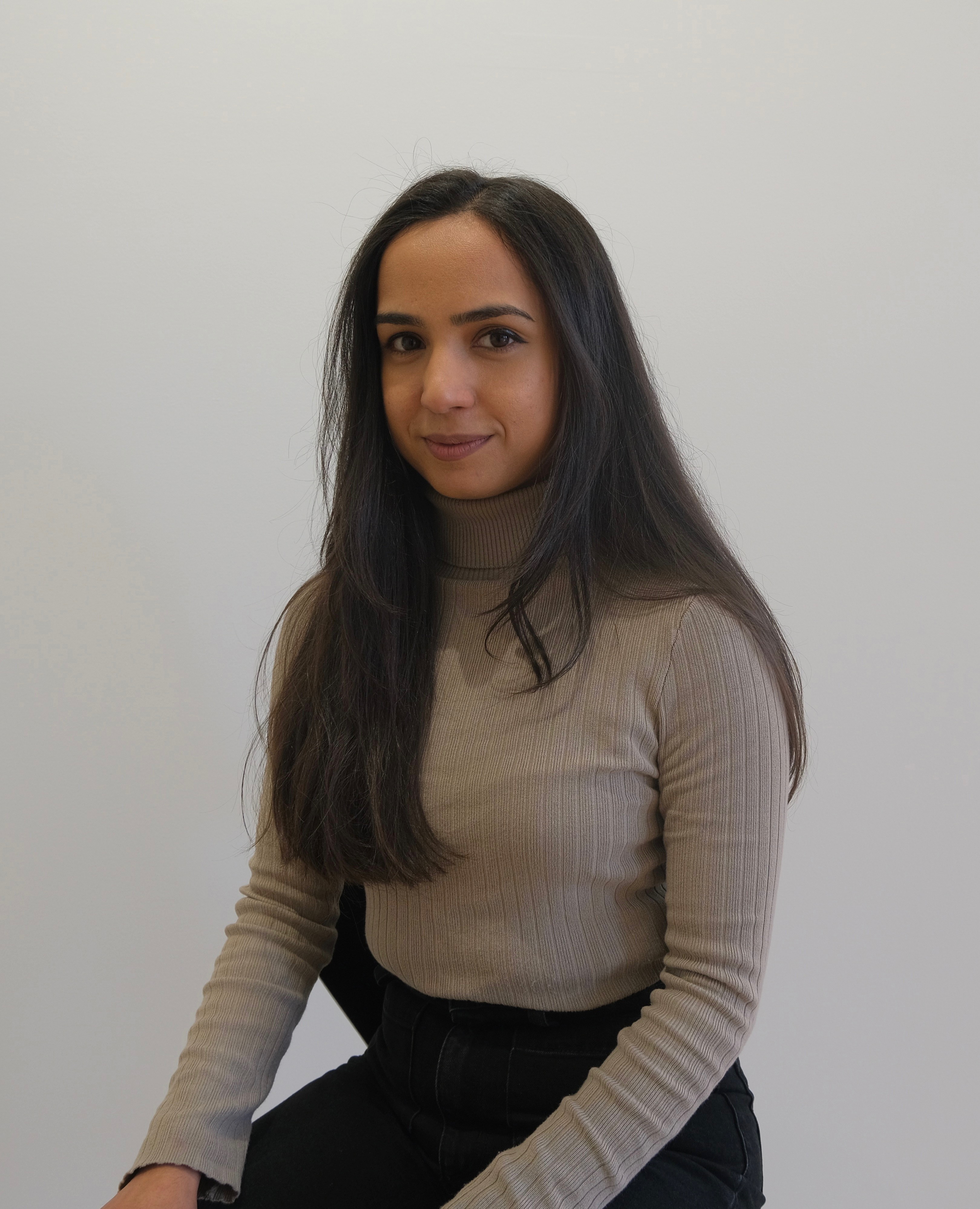 A photographic portrait of a woman with long black hair. She is sitting and wears a grey jumper. 