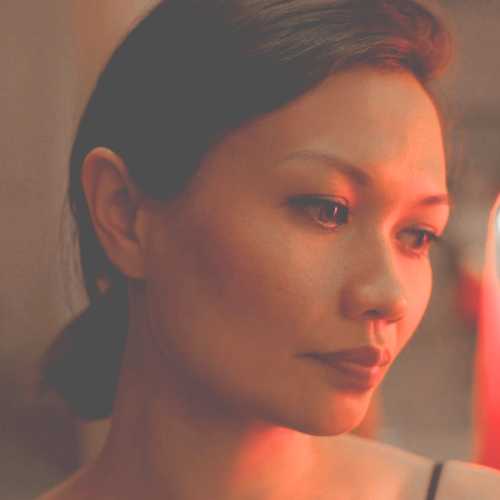 A woman with her hair tied back lit in soft red and orange lights staring to her side