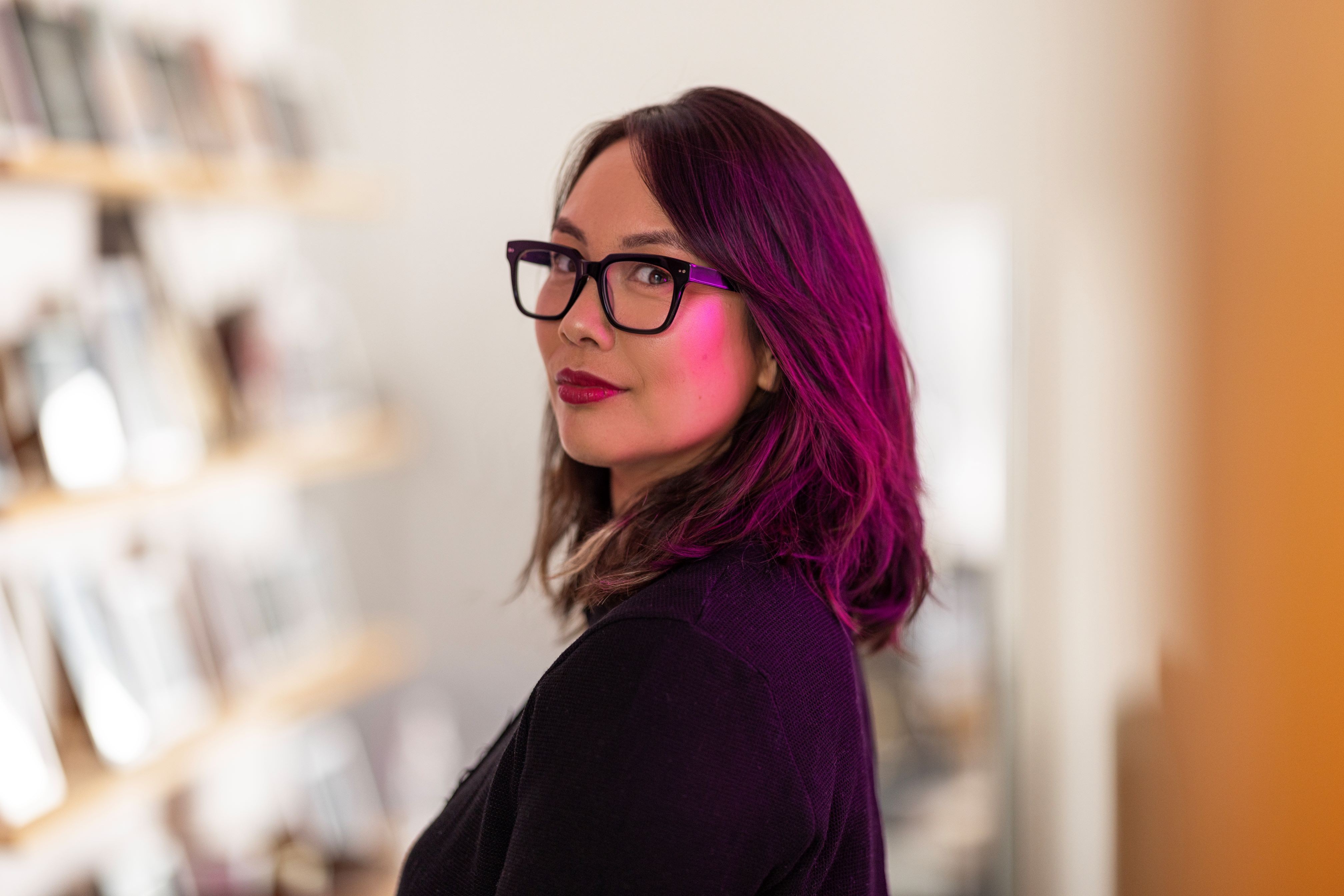 Side profile of a woman wearing glasses and red lipstick, looking directly at the camera