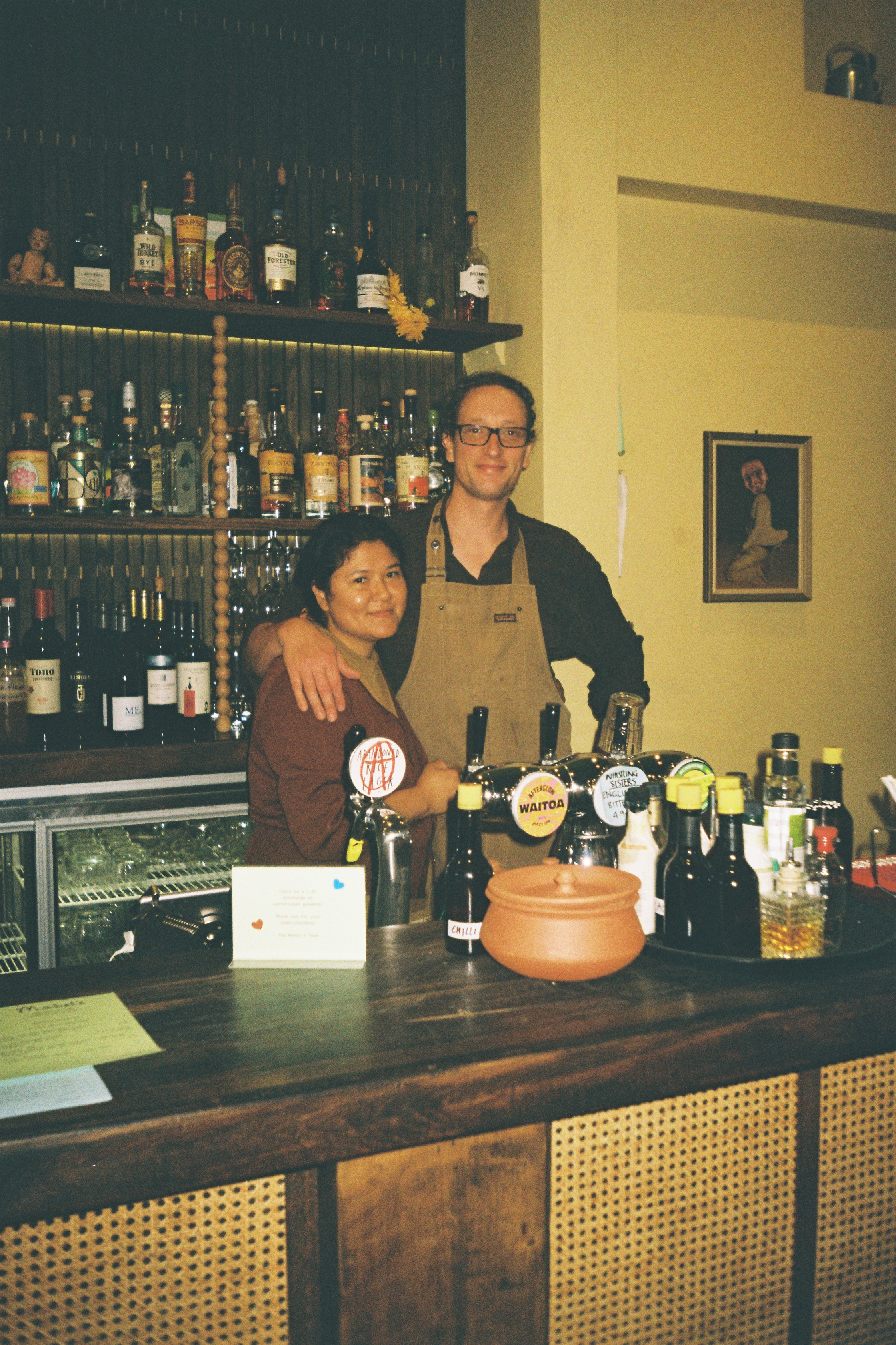 Marlar and Ian standing behind a bar with their arms around us.