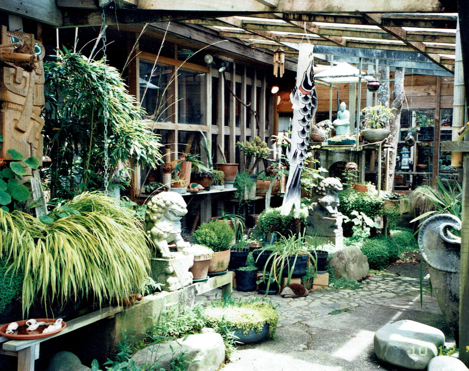 Sculptures and plants sit underneath an awning at the entrance to a wooden house