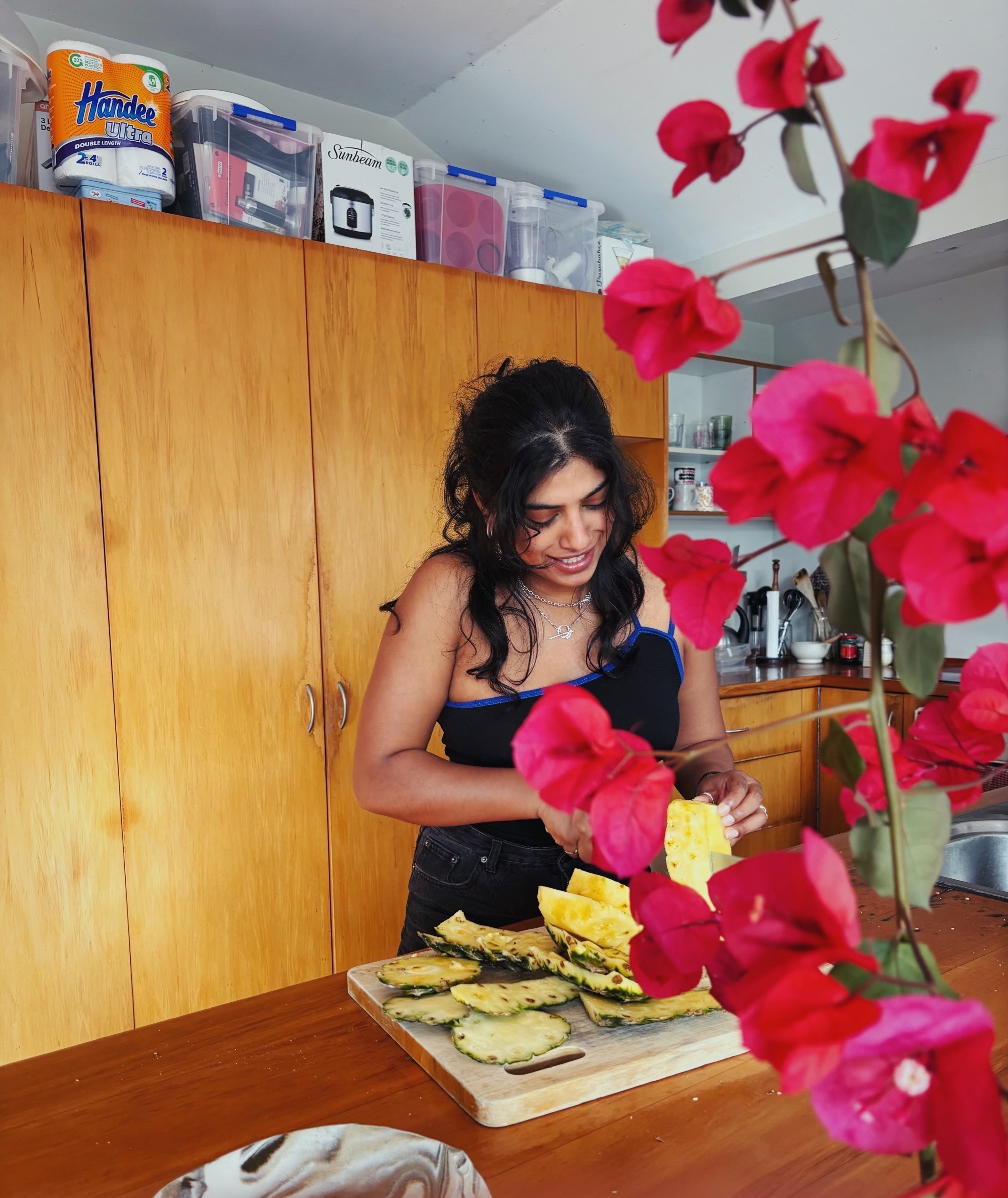 Dilohana has long curly dark hair and is cutting a pineapple in a kitchen.