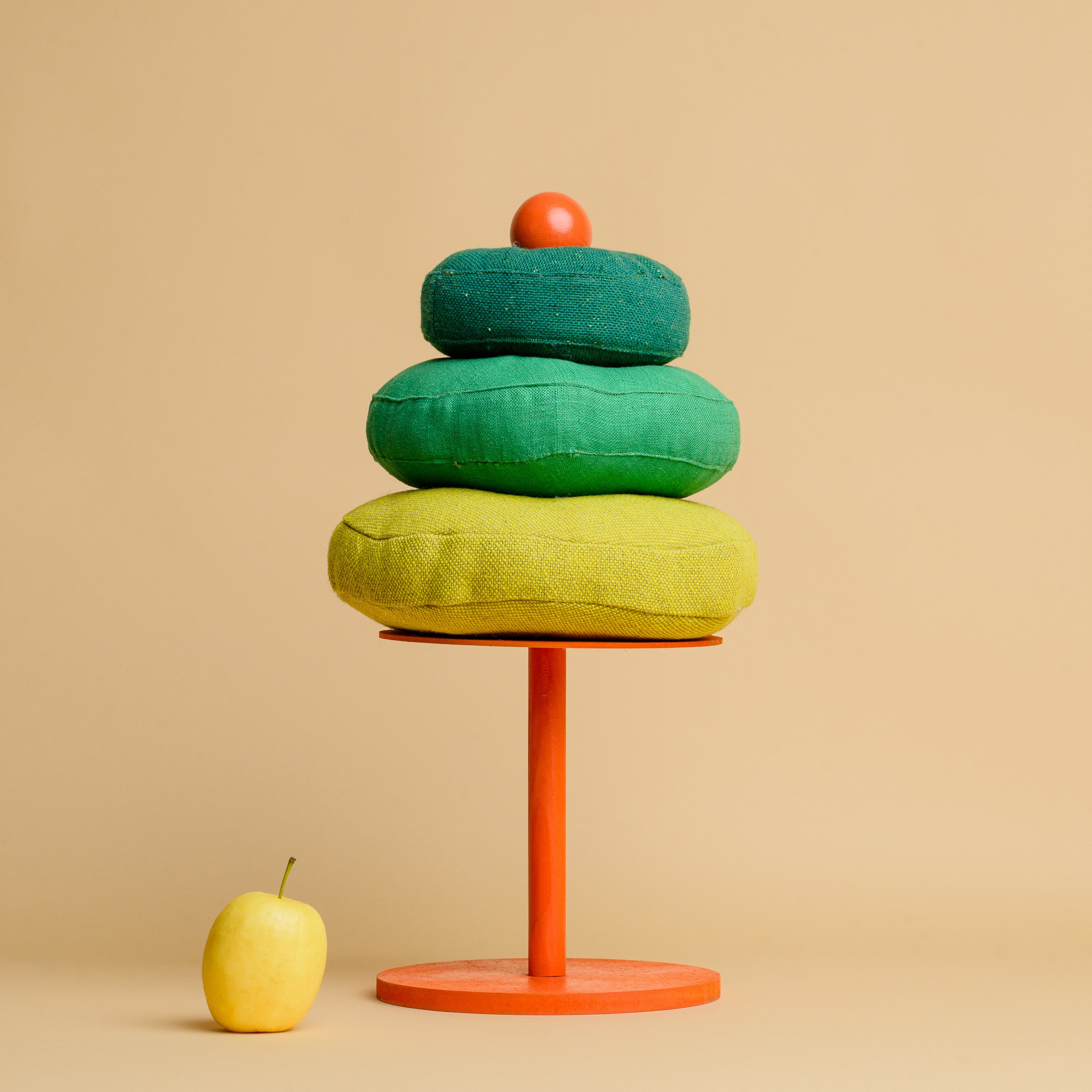 A stack of three round green cushions on an orange plinth, resembling a tree