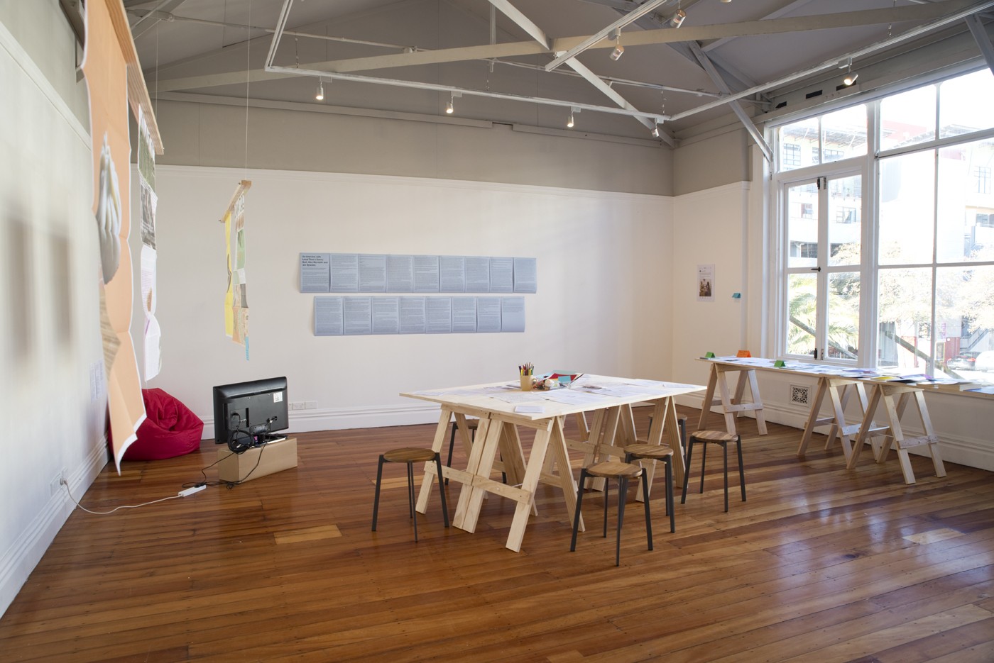 A gallery filled with trestle tables, stools and posters.