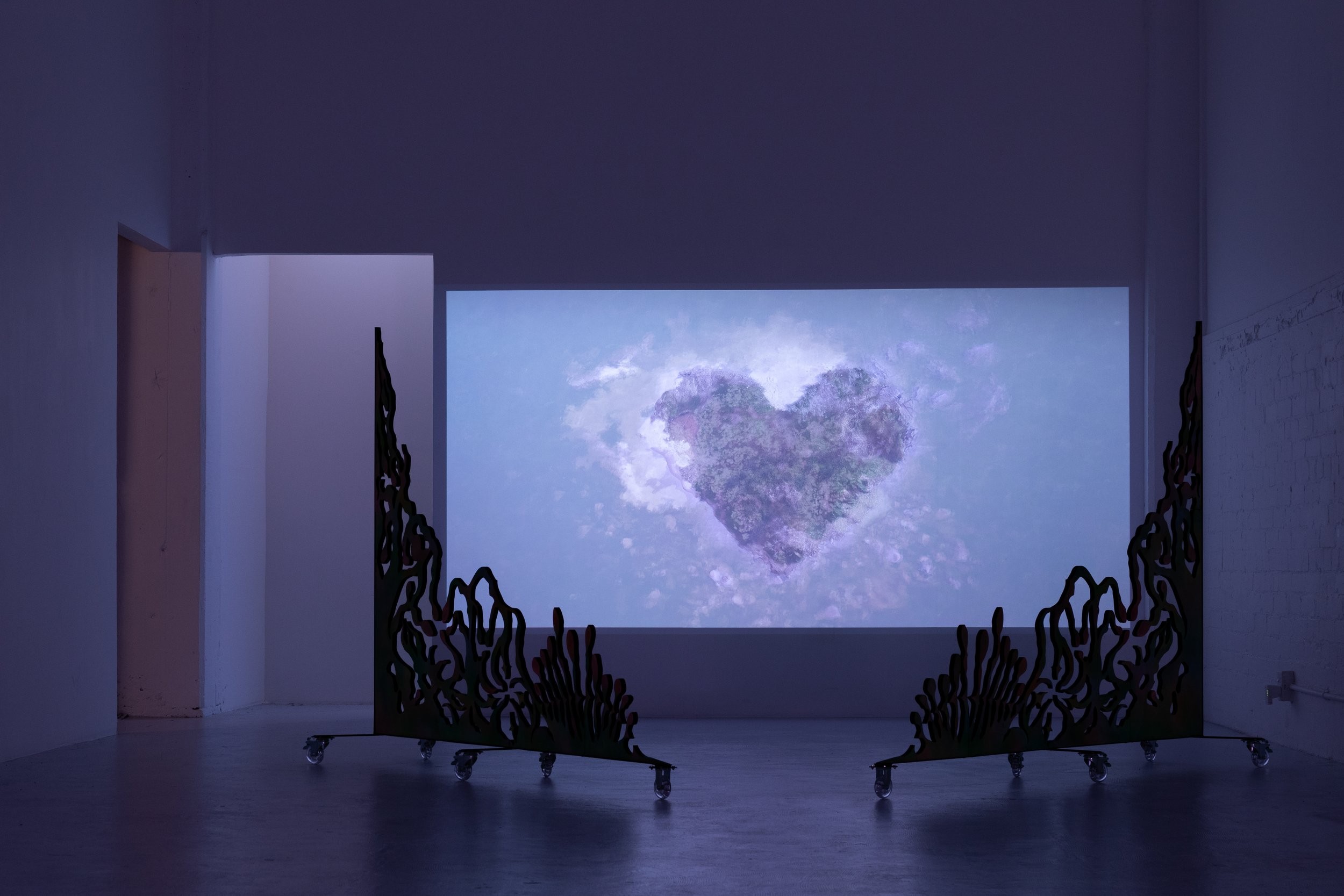 A projection of a dreamy purple heart surrounded by clouds, bordered in the space by two intricate gates on wheels