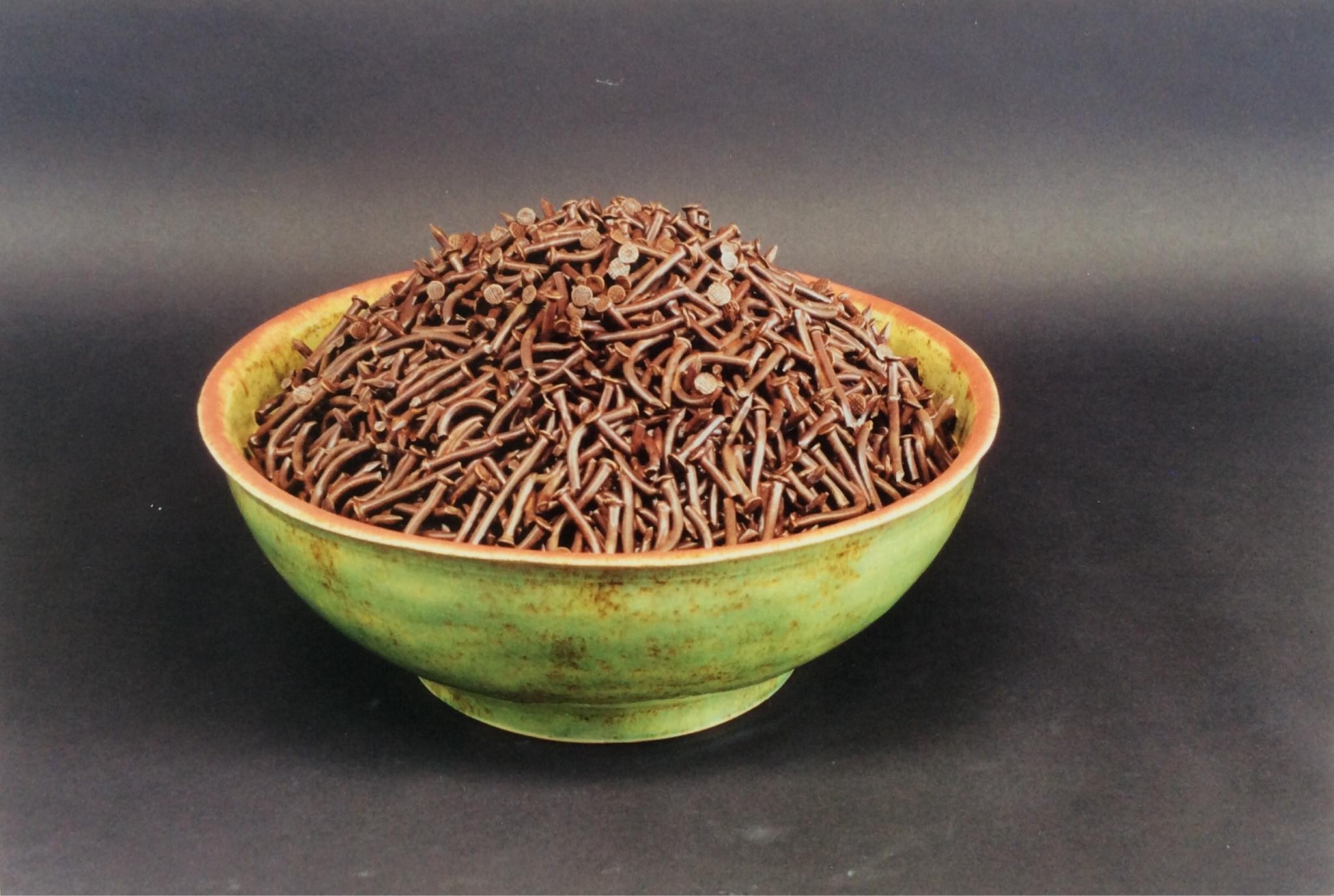 A green bowl full of bronze nails