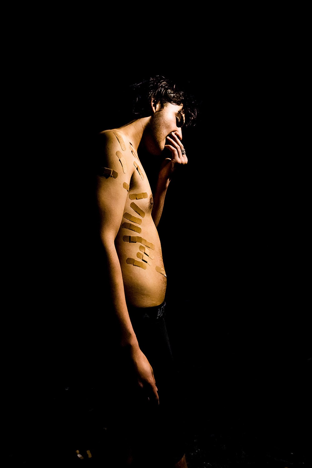 A skinny half-naked man covered in plasters posing with dramatic lighting
