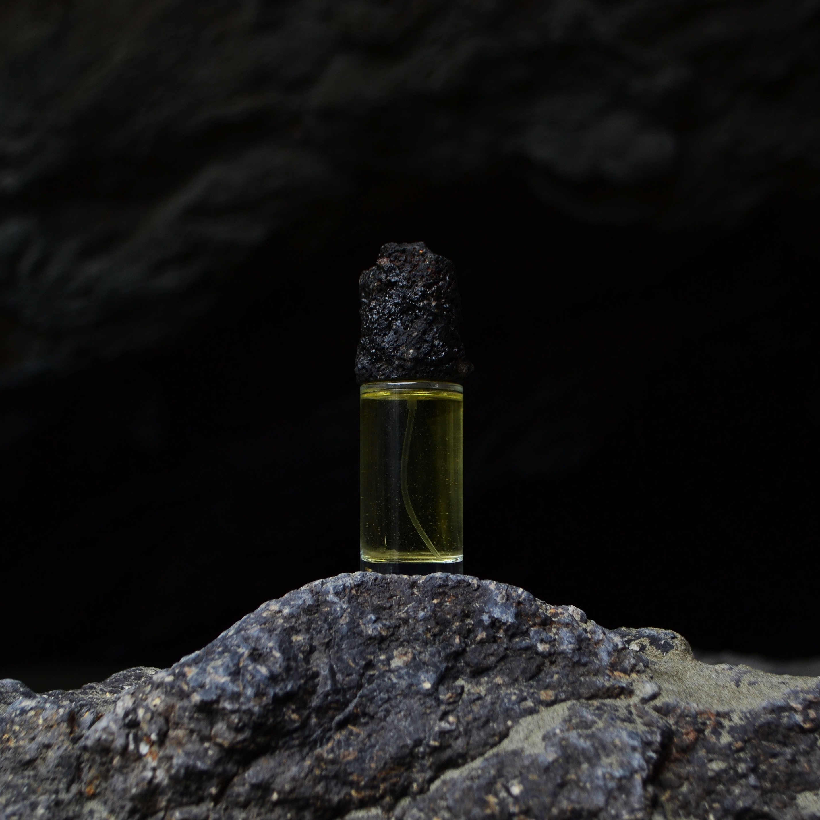 Small perfume bottle sitting on a rock with a lid made from the rock.