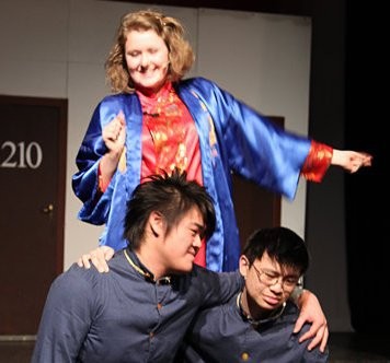 Two Chinese teenagers with their arms around each other with another student behind them on stage.