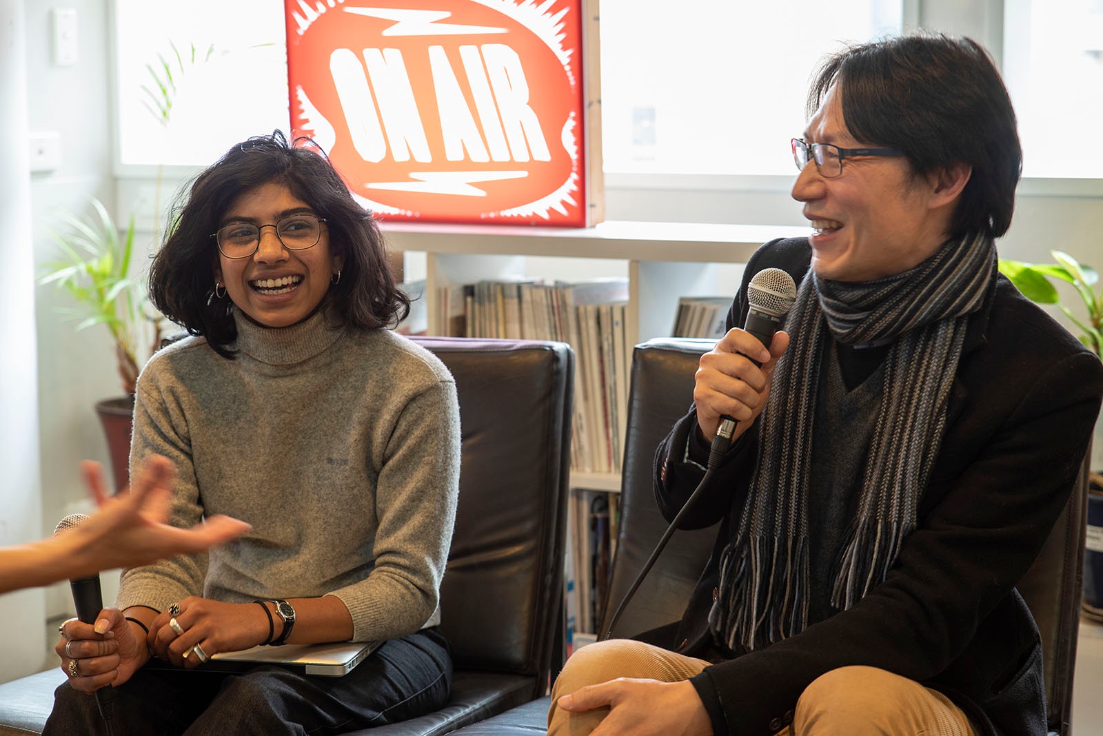 Dilohana and Jon sit next to each other, laughing and holding microphones. An 'on air' sign is lit up in the background.