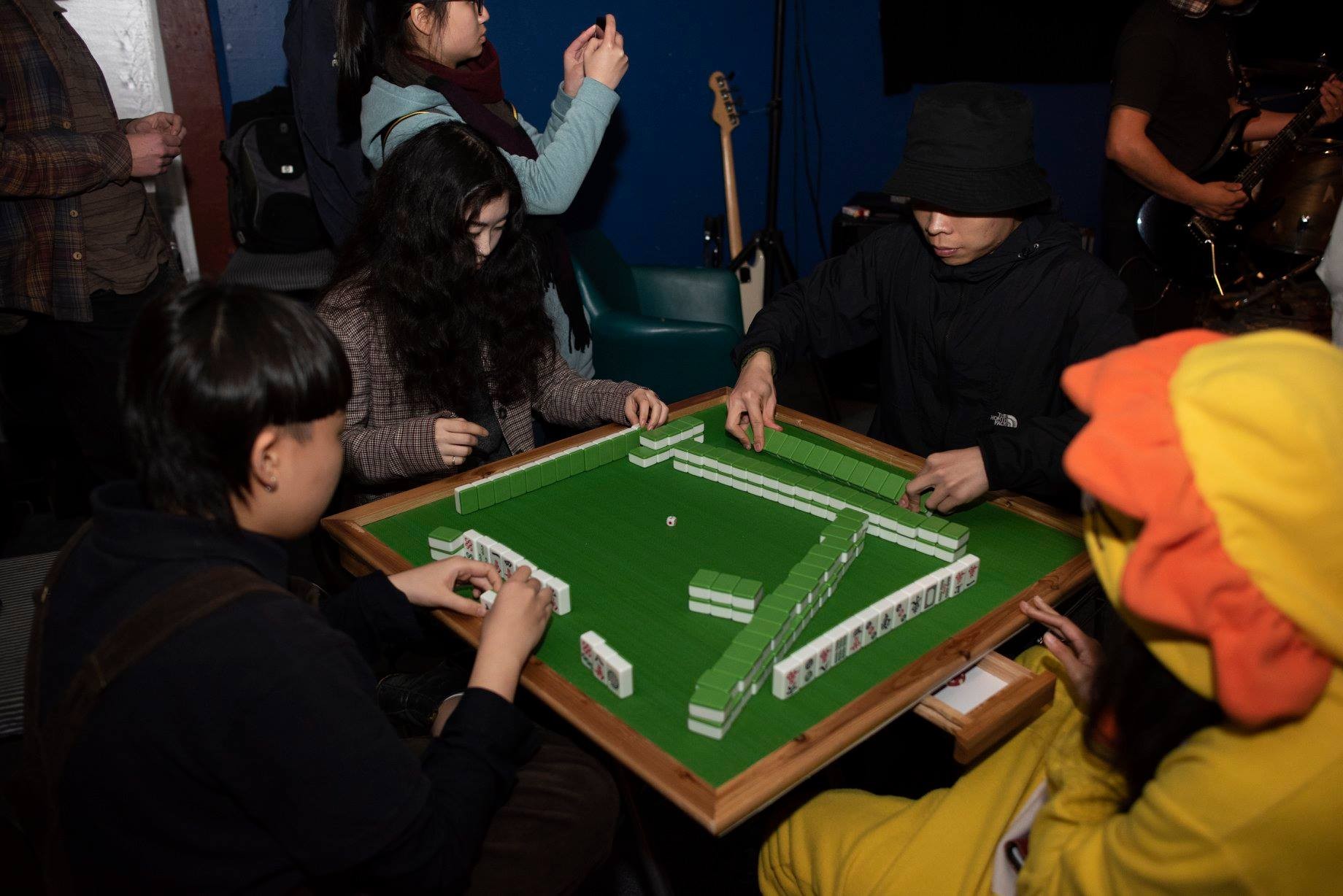 Four people playing mahjong in a crowded room