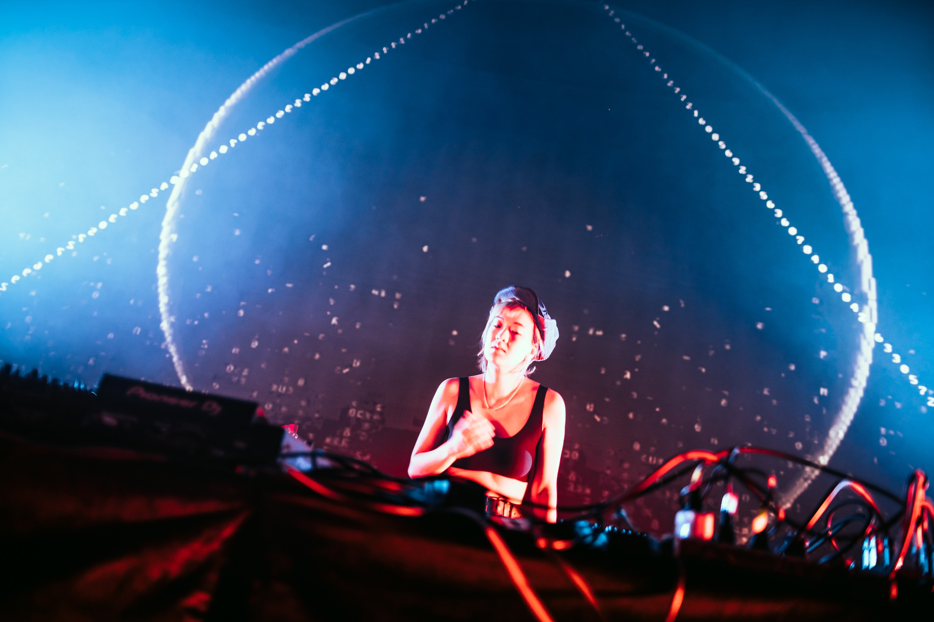 Dramatic lighting hits a DJ standing in front of a projector screen