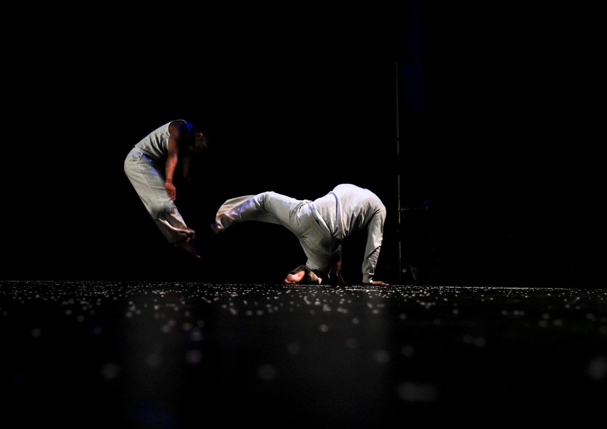 Action photo of a dance performance with one performer jumping in the air while another is posed on the ground