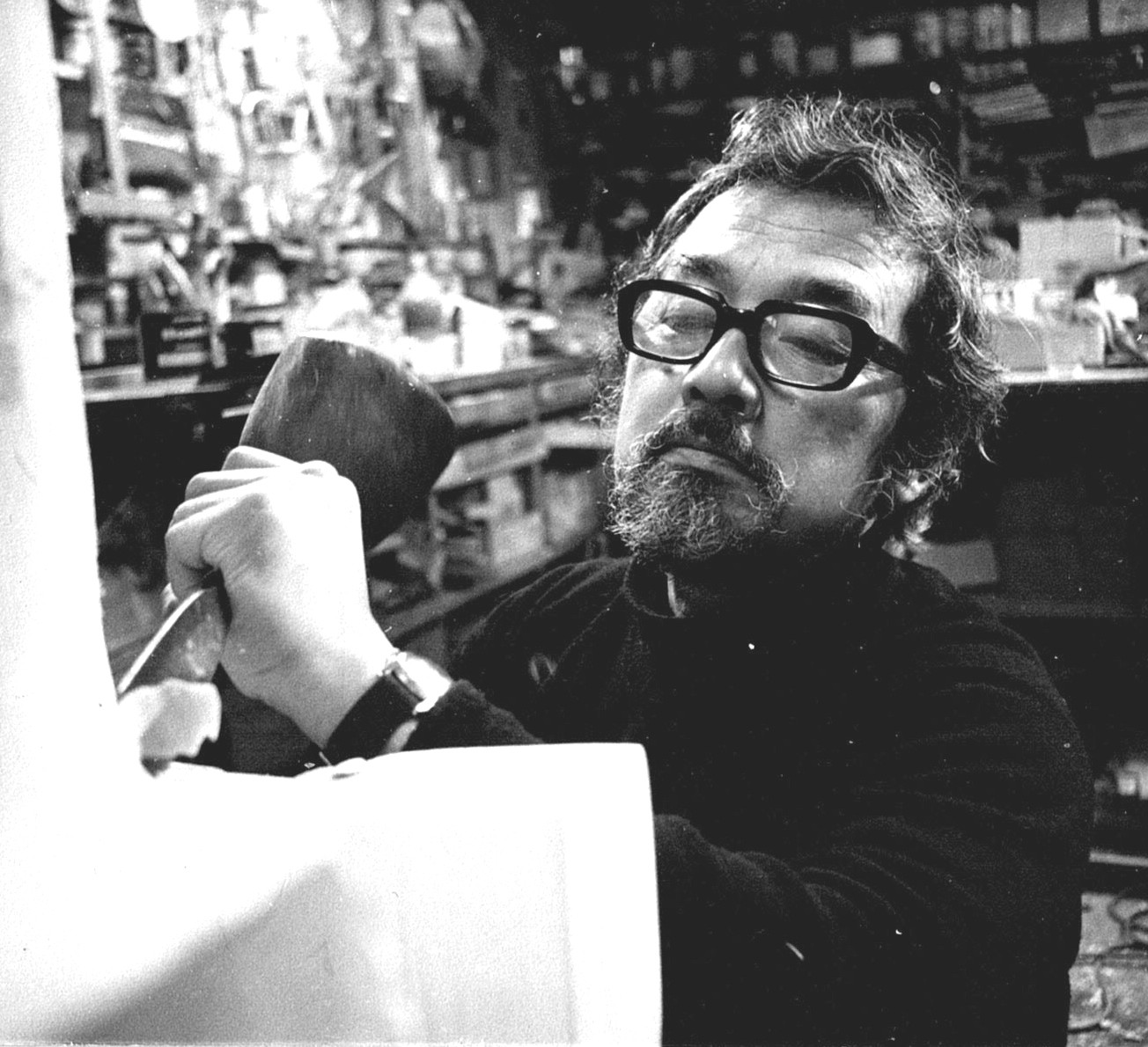 Black and white photo of a bearded man in glasses using a mallet and chisel