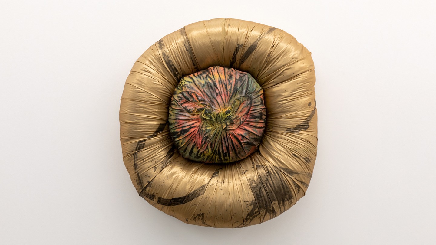 A tightly stuffed doughnut with a central stuffed object inside, almost resembling a bellybutton, painted bronze