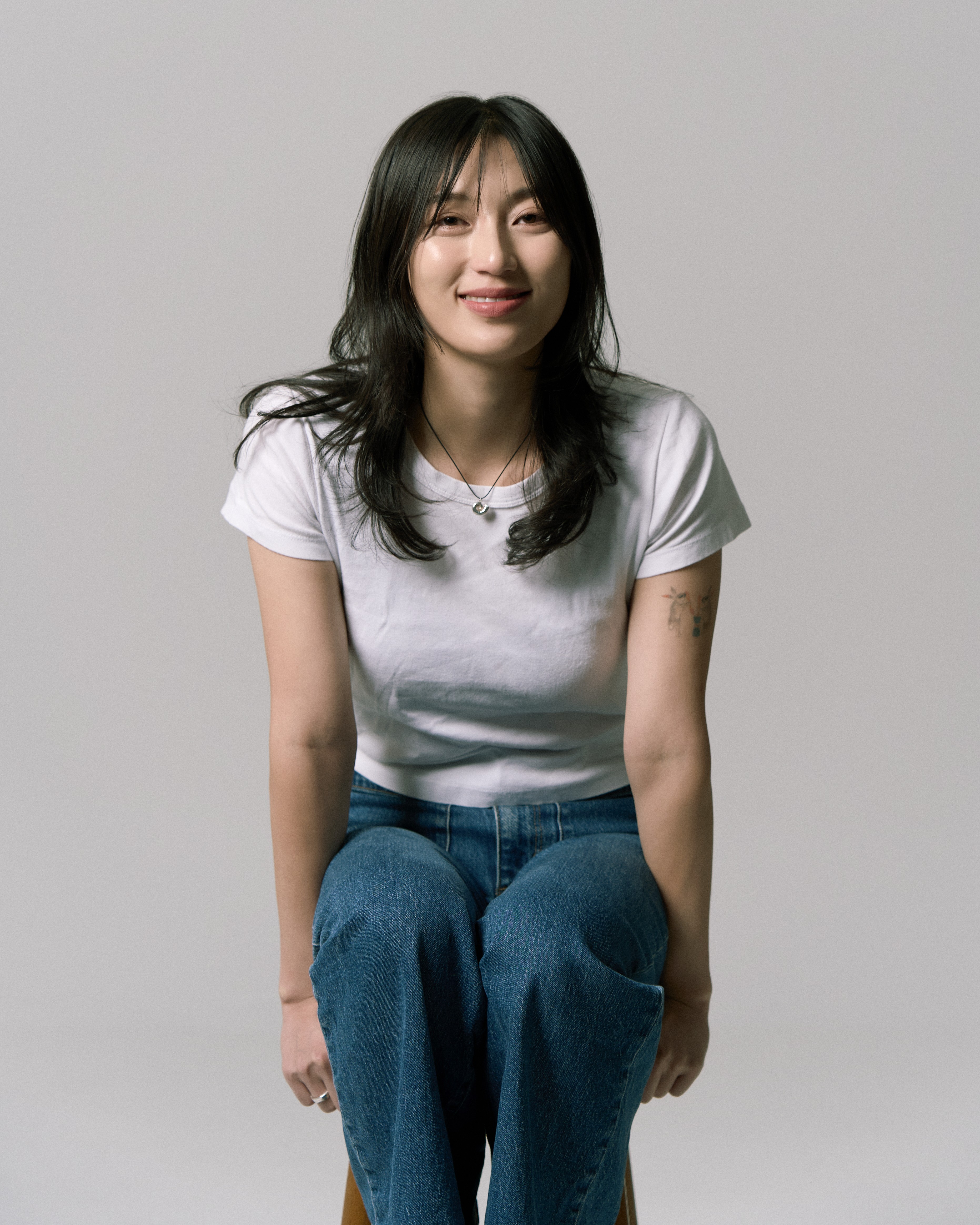 Long haired woman sitting on a stool looking into the camera smiling.