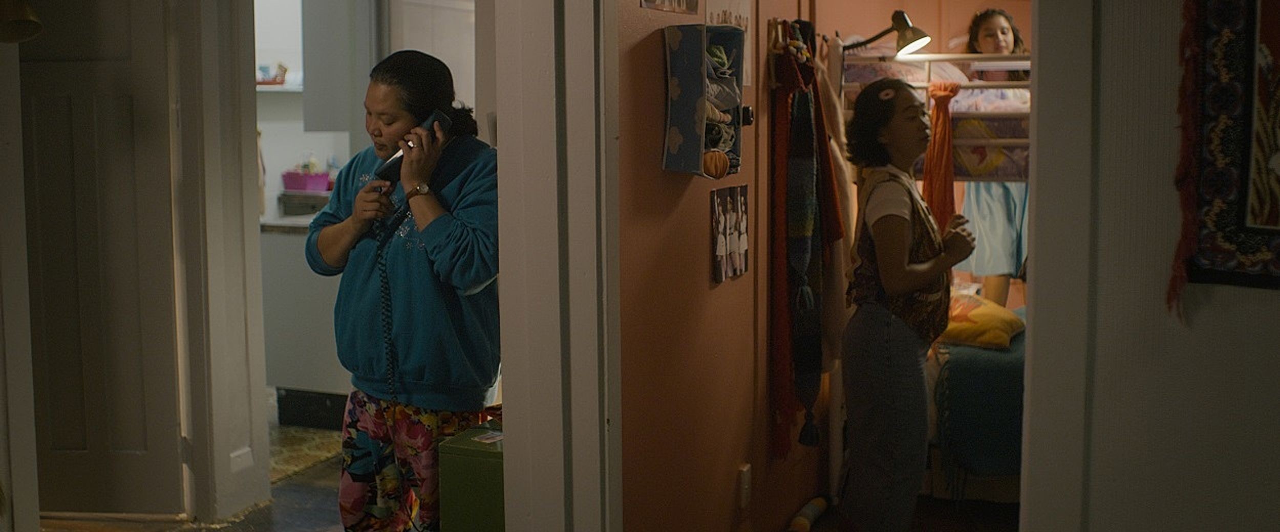 A still from a movie that is split in 2 parts - left part has a mature person in house clothes talking on the phone, the right part has young people looking dressed and ready to go out