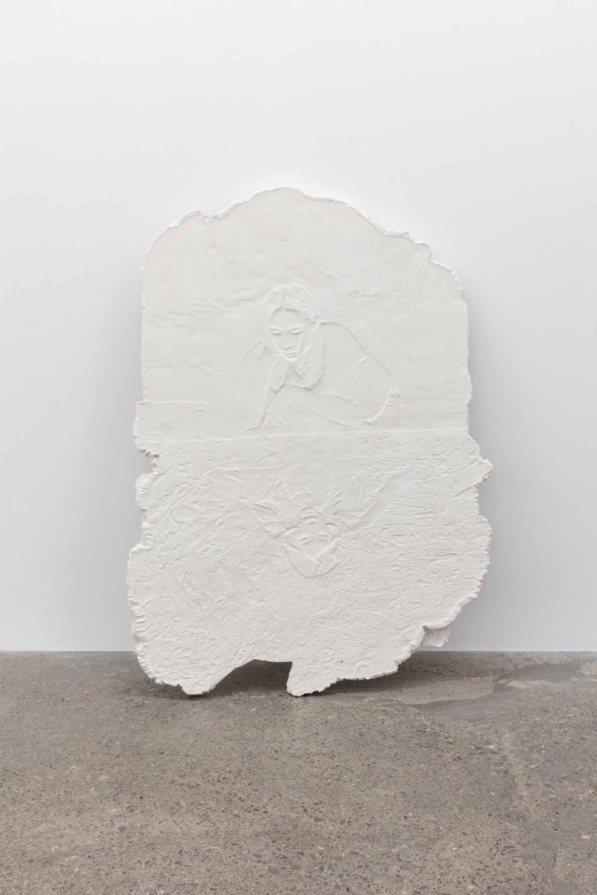 a small flat tablet of plaster with rough edges with a portrait (and its reflection, as though looking down onto a mirrored table) carved lightly into the surface.
