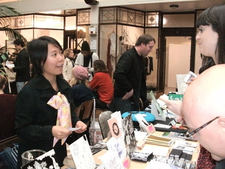 A person manning a zine table and talking to a customer 