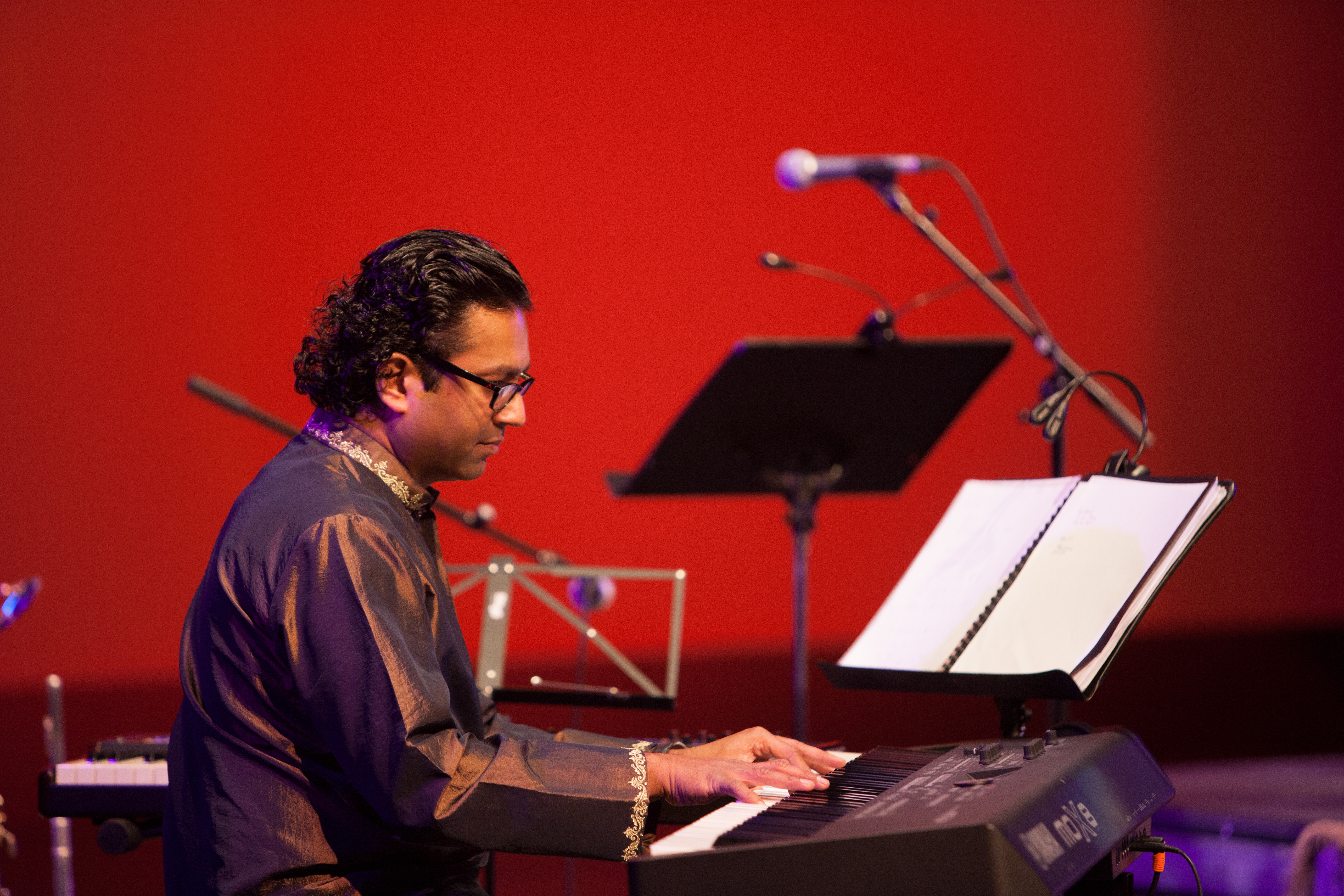 A person sitting at a keyboard with music stands and microphones in the background