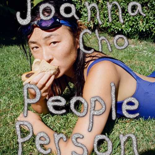 Photo of an Asian woman lying on the grass in a blue swimsuit wearing goggles and eating a sandwich.