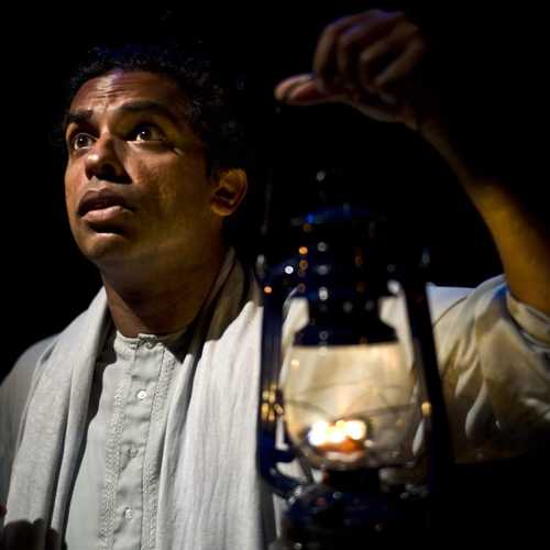 A man in white robes holds a lantern up