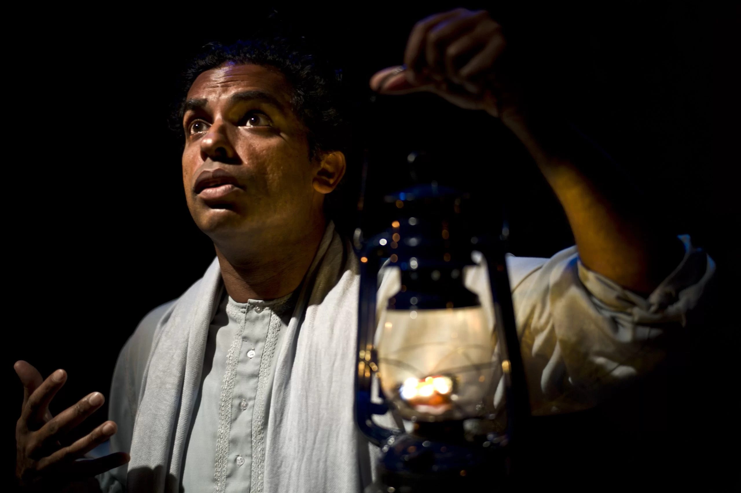 A man in white robes holds a lantern up