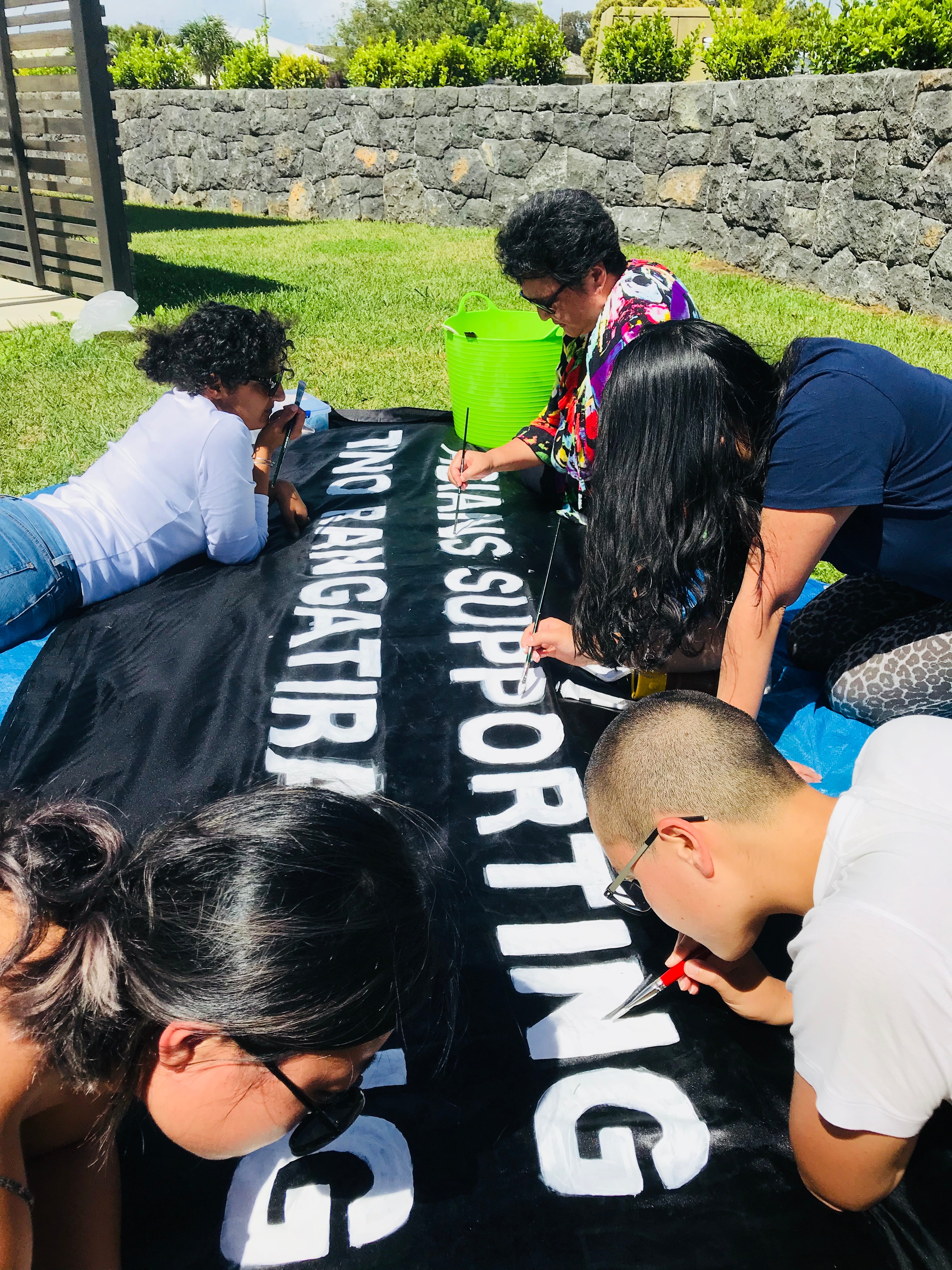 A group of people painting a black banner with white text
