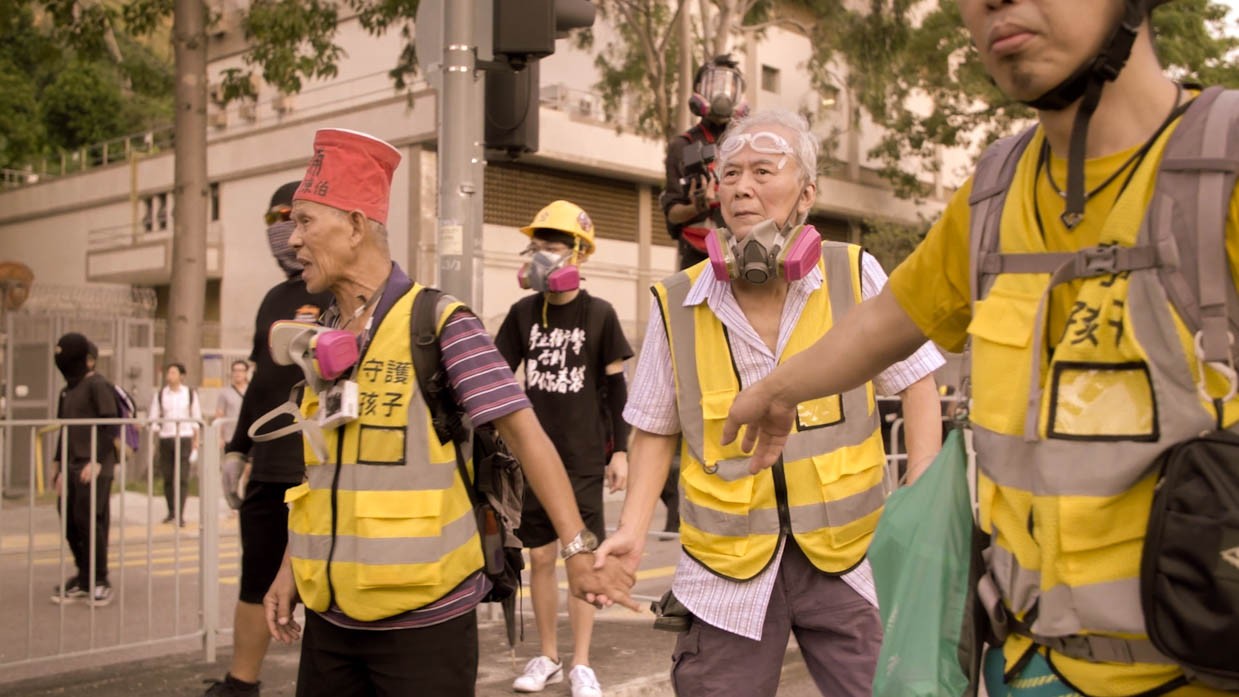 Two elderly men wear bright yellow safety vests, gas masks and goggles, as part of a Hong Kong protest.