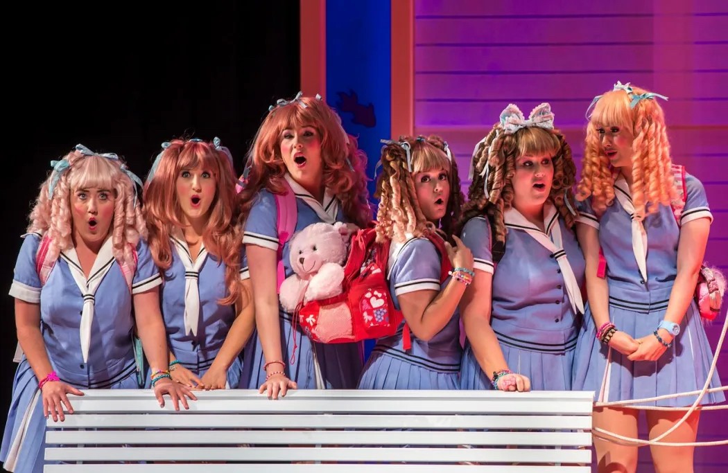 Photograph of women singing, wearing wigs and school uniforms.