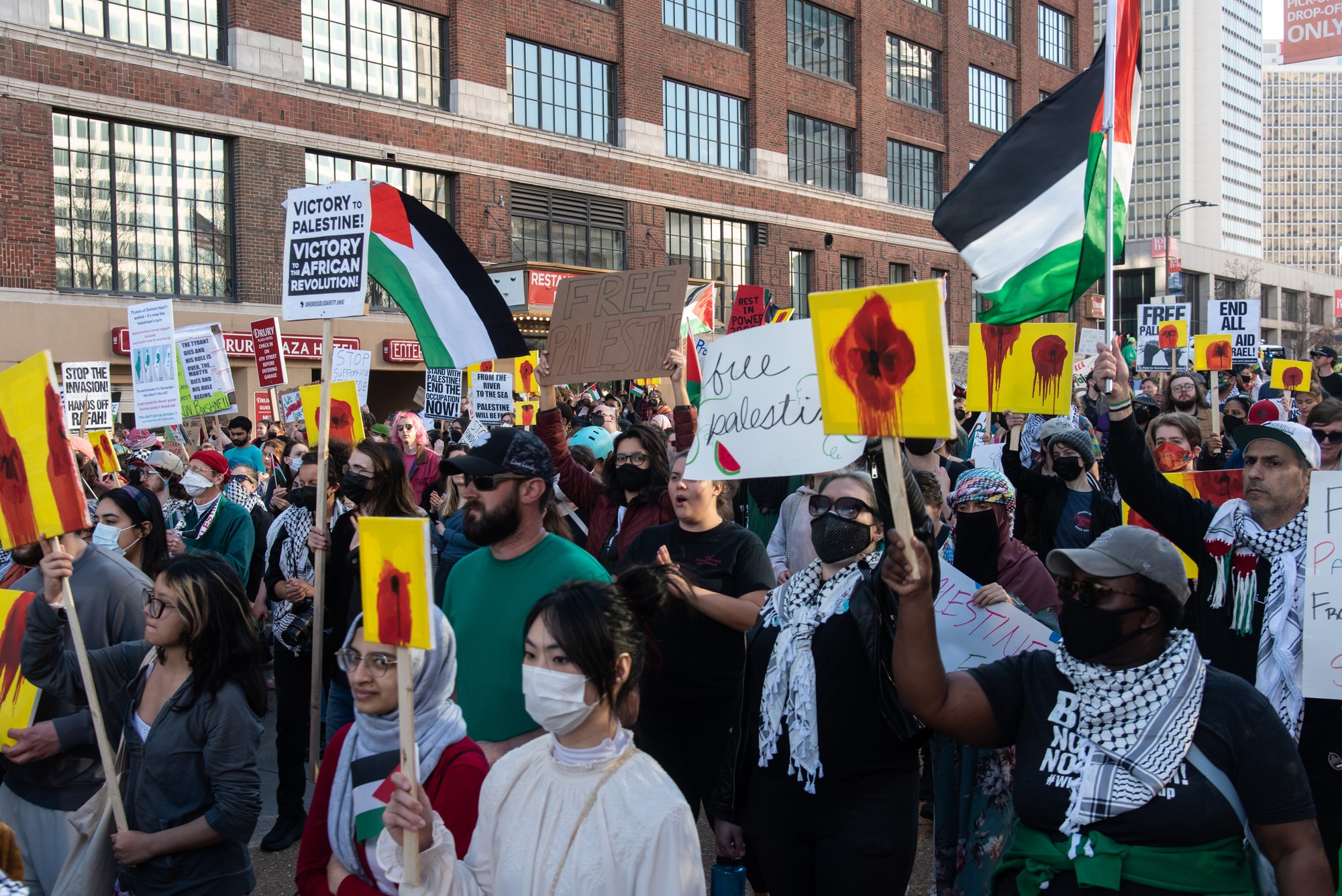 A protest moves down a street, with some protestors holding poppy paintings as placards.