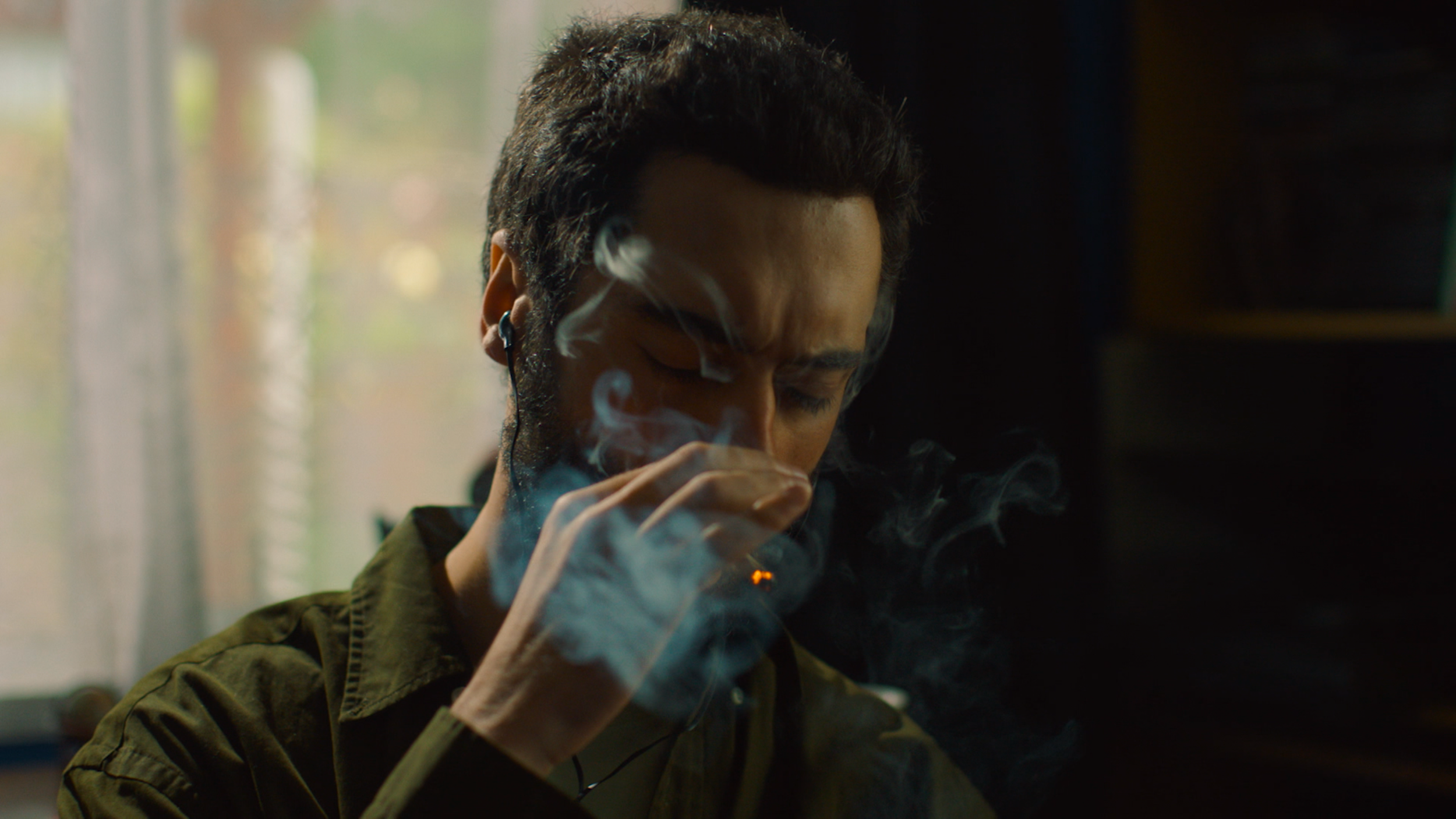 A man with closed eyes smokes indoors as swirls of smoke drift around his face.
