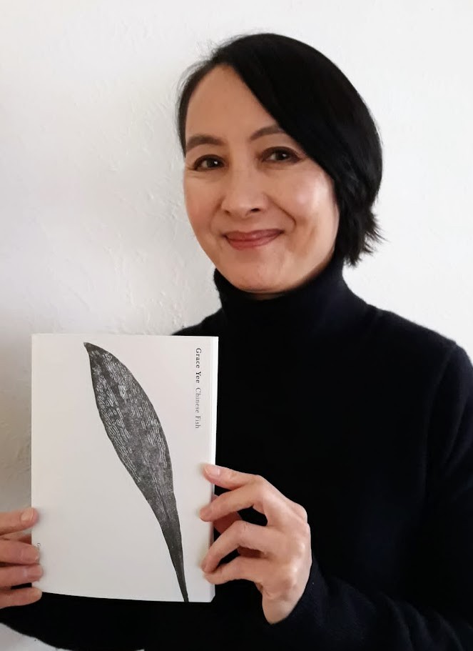 Grace Yee has a black bob and is smiling while holding up a copy of her book. 