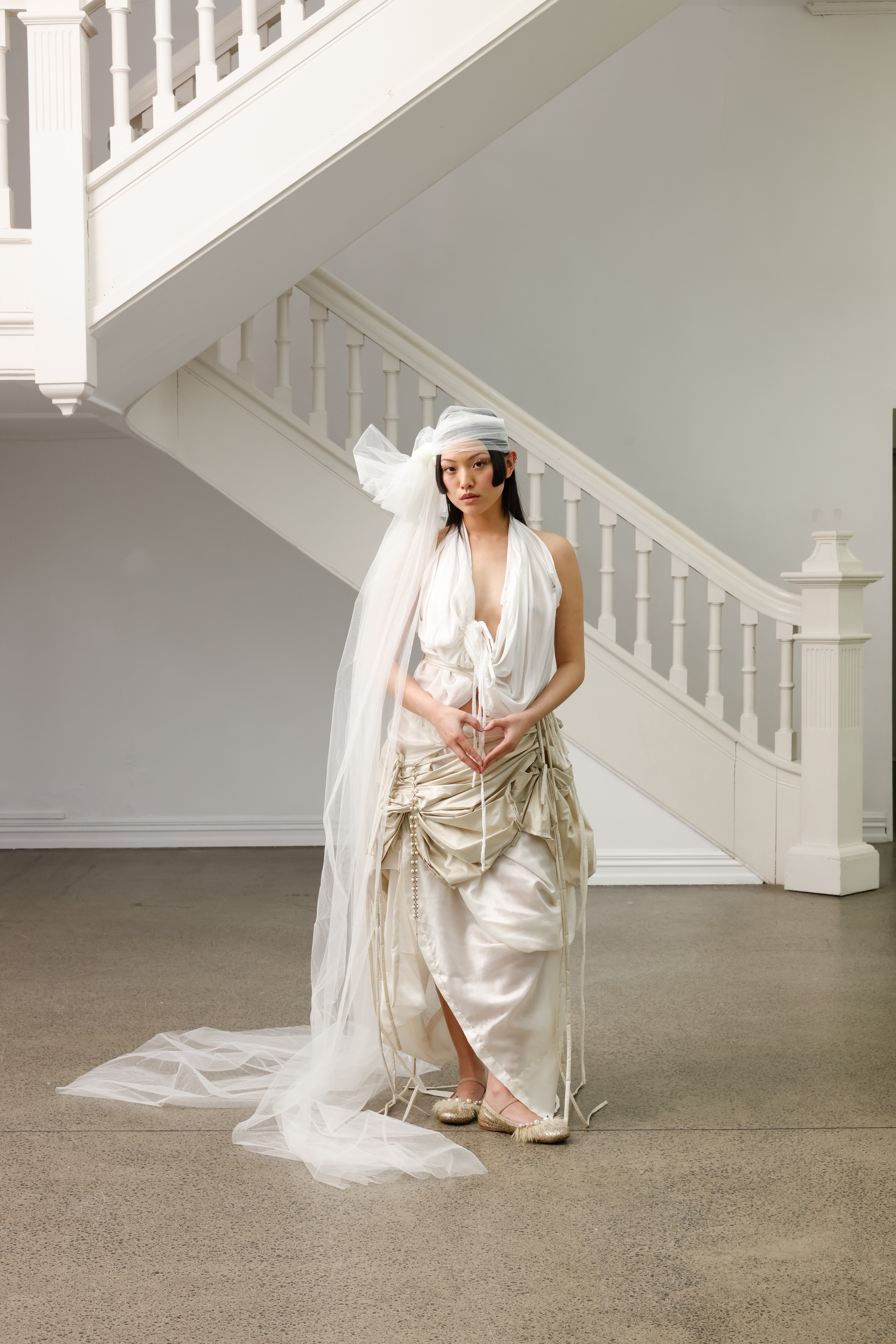 A model in a cream and white gathered wedding gown with lots of volume stands in front of a staircase