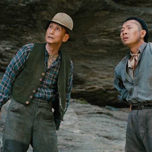 In a scene from “Illustrious Energy”, two Chinese men stand with their backs against a rocky cliff face, looking into the distance