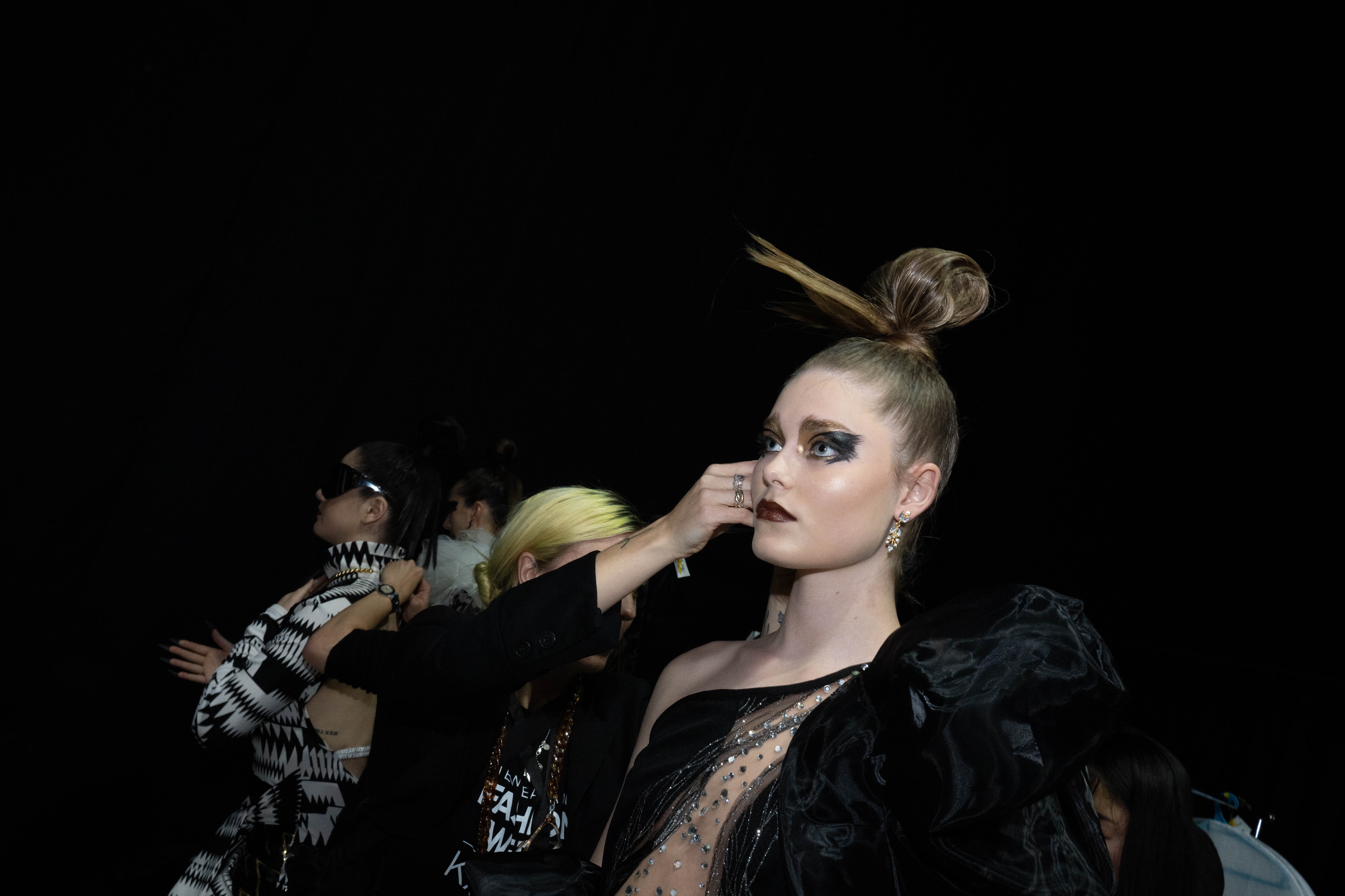 A woman with a high top knot getting make-up applied to her face