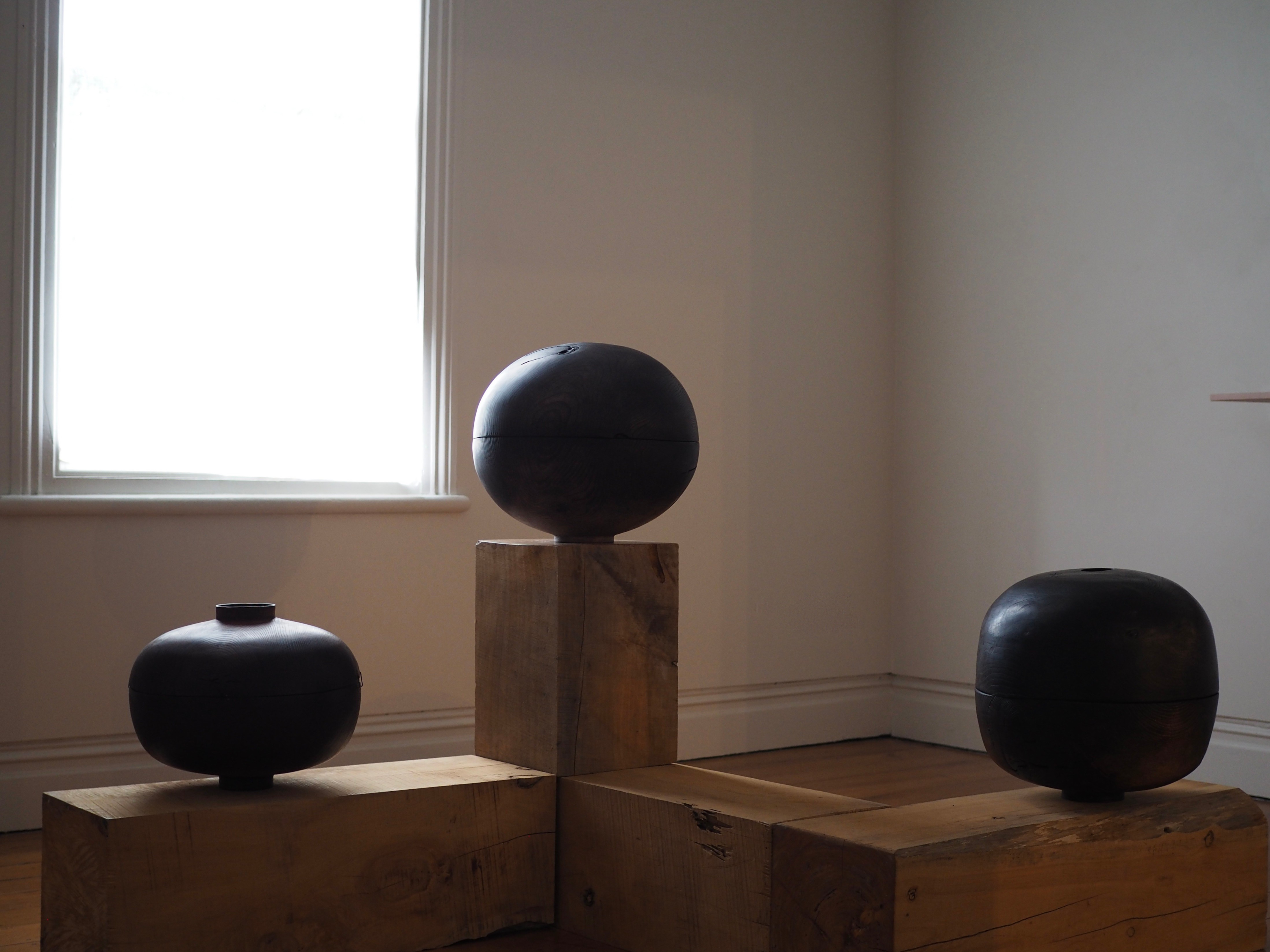 Three elongated rounded wooden objects displayed on plinths