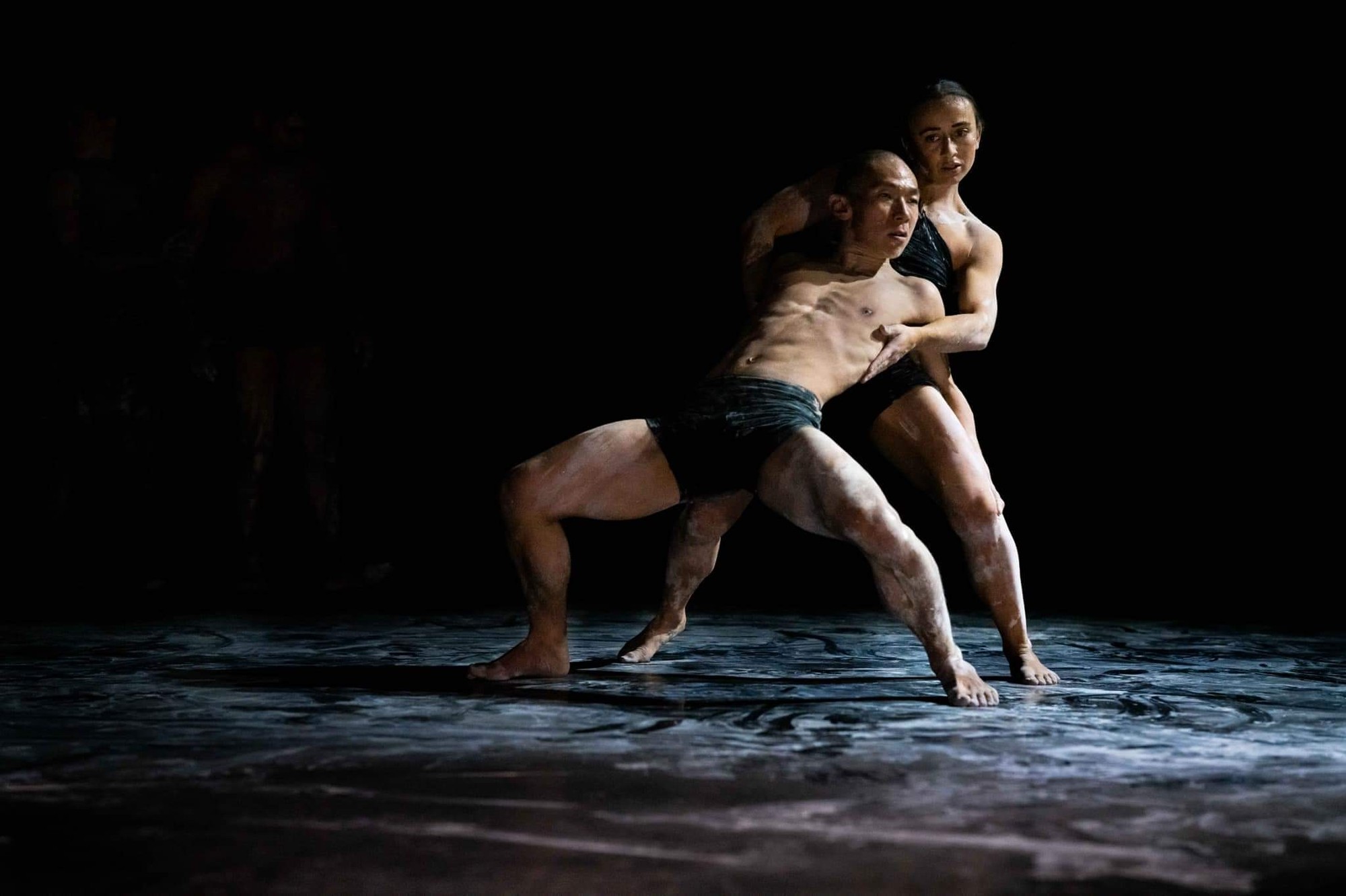 Two dancers on a dark, chalky stage.