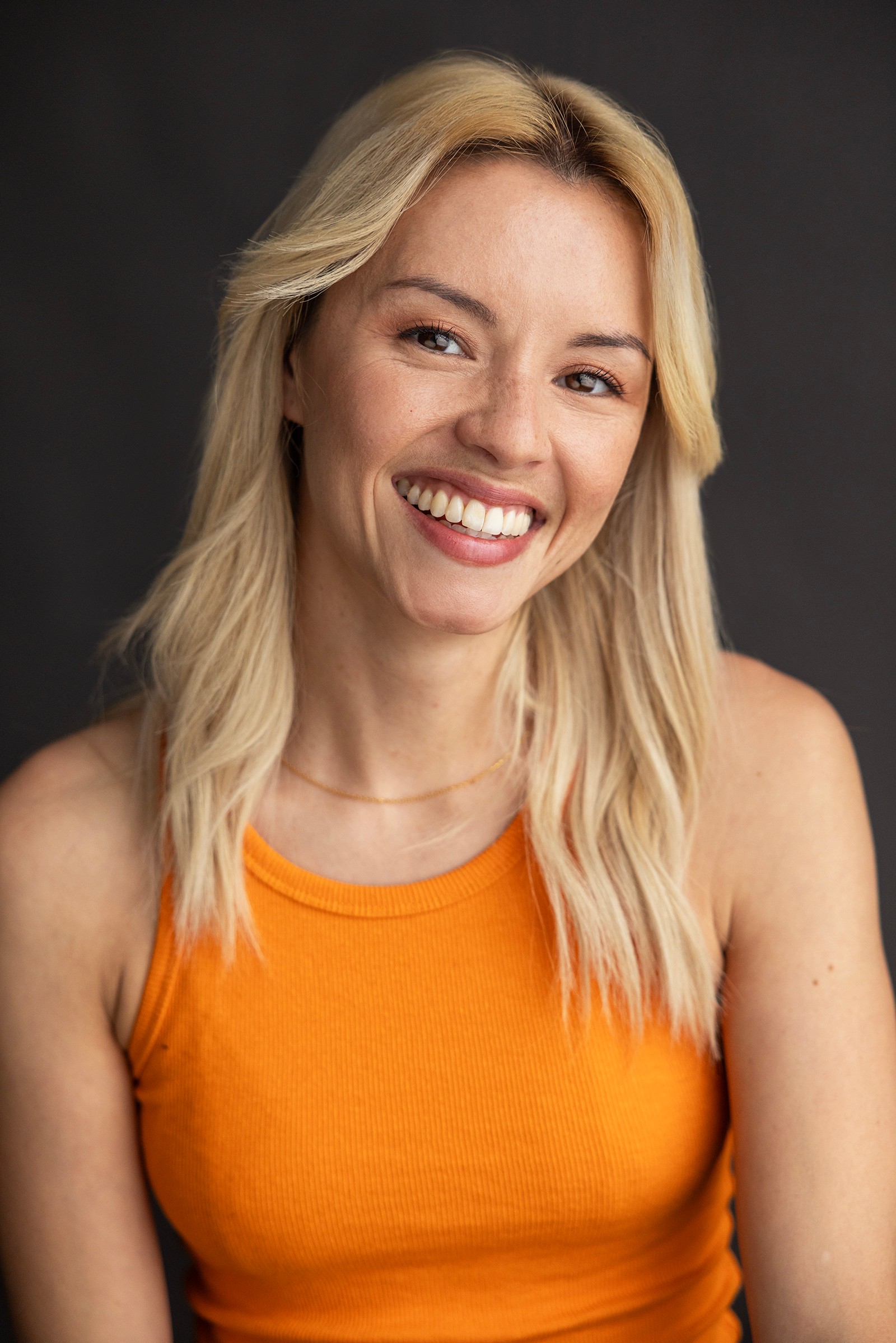 A woman with bleached-blonde shoulder-length hair and an orange singlet smiling at the camera.