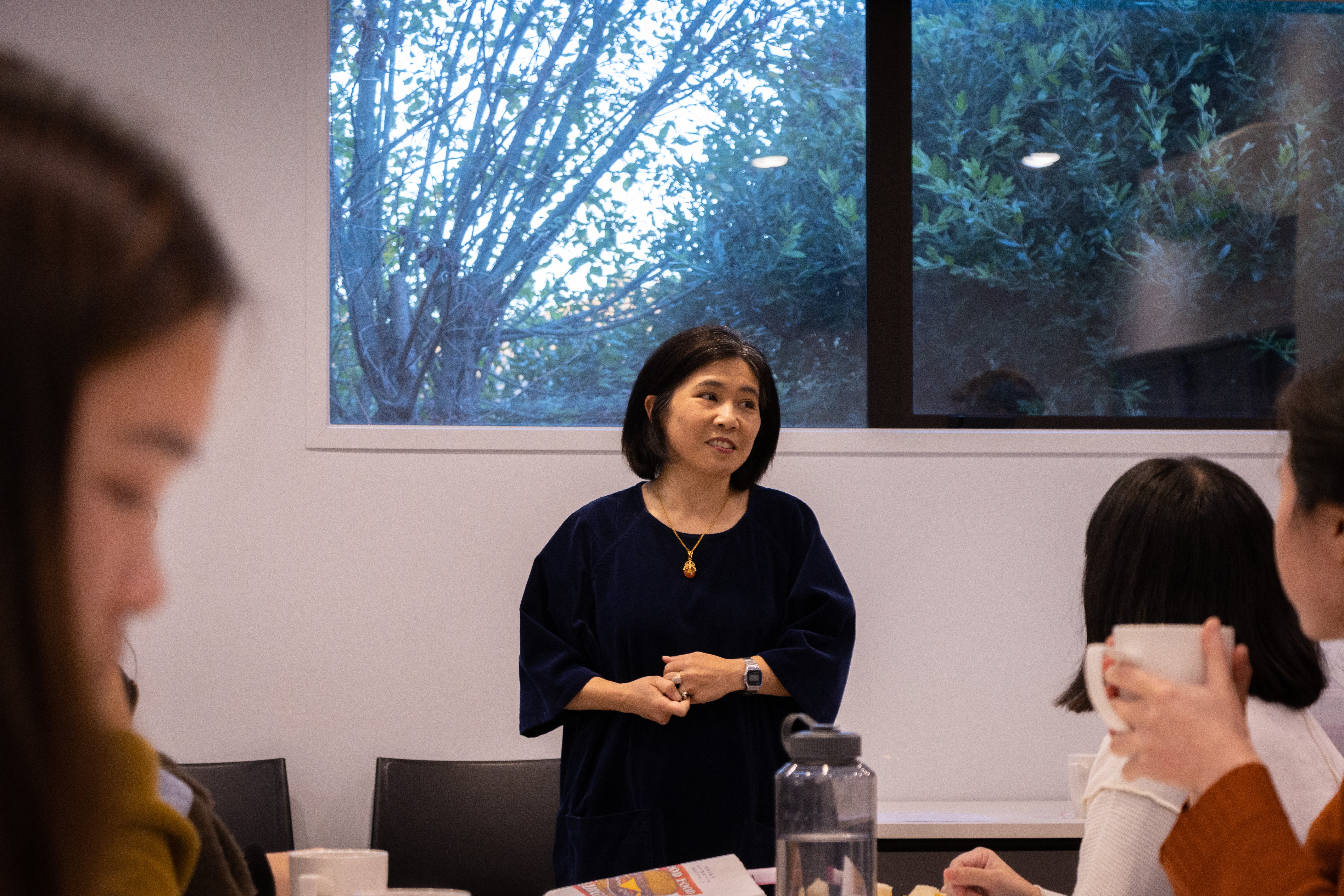 A woman with a black bob and a black dress addressing the group